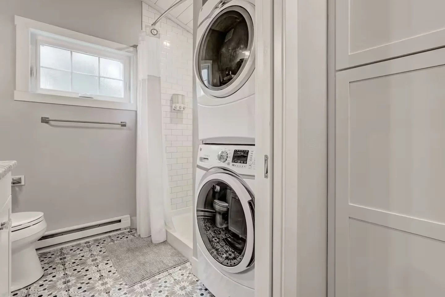 Bathroom and in-unit laundry area inside a detached accessory dwelling unit in Colorado Springs, Colorado, featuring a stacked washer and dryer, subway tile shower, and patterned tile flooring.