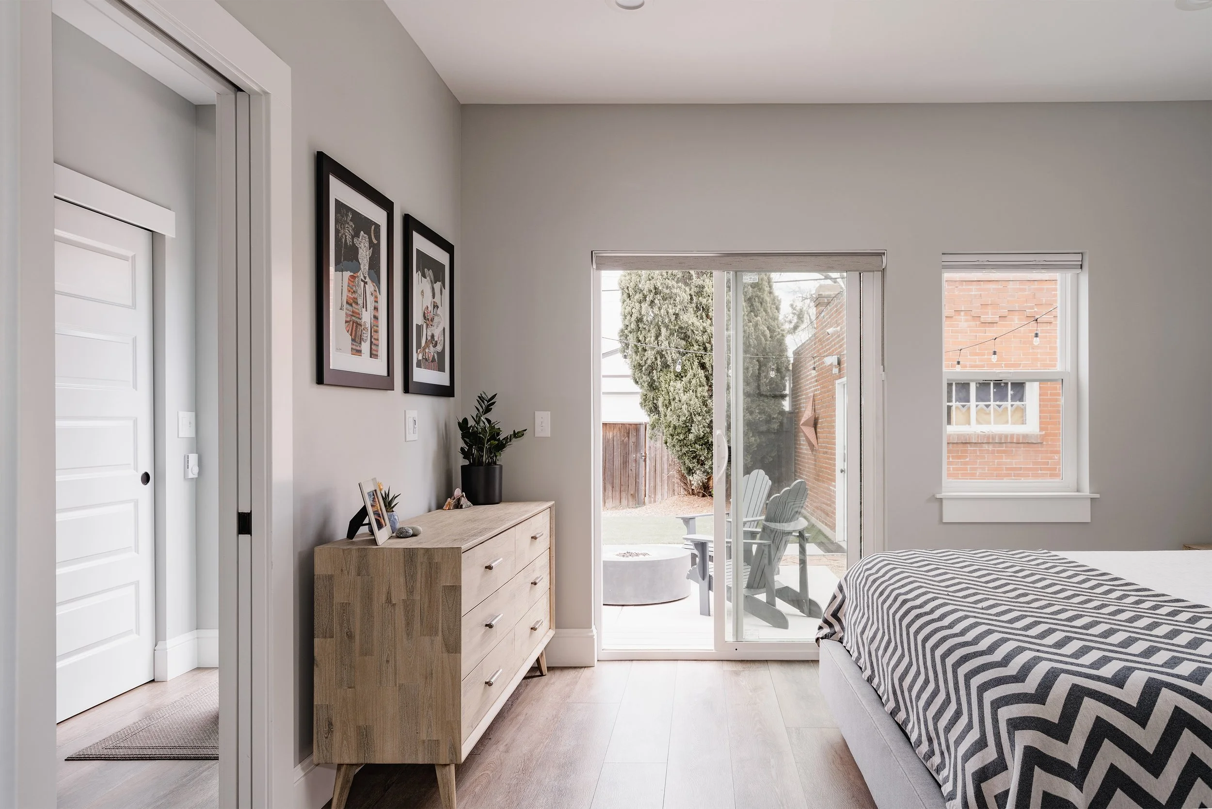 Primary bedroom inside a Denver home addition featuring wood flooring, a sliding glass door to the backyard patio, and simple modern finishes built by Prenvalley Builders.