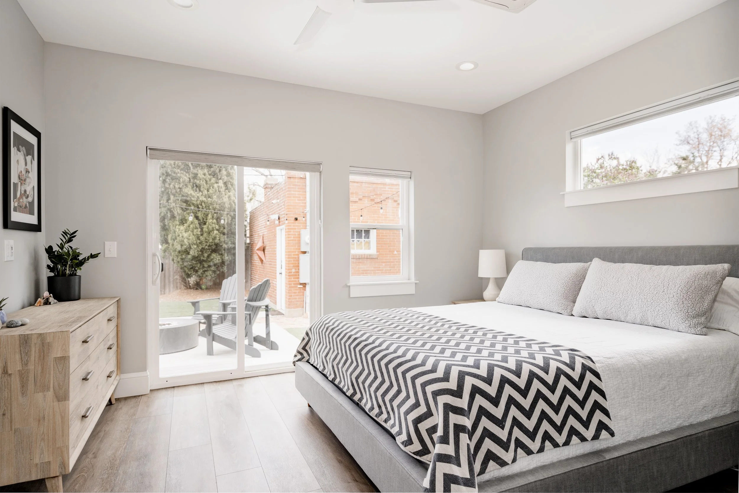 Primary bedroom inside a Denver home addition featuring a sliding glass door to the backyard, large windows, wood flooring, and simple modern finishes by Prenvalley Builders.