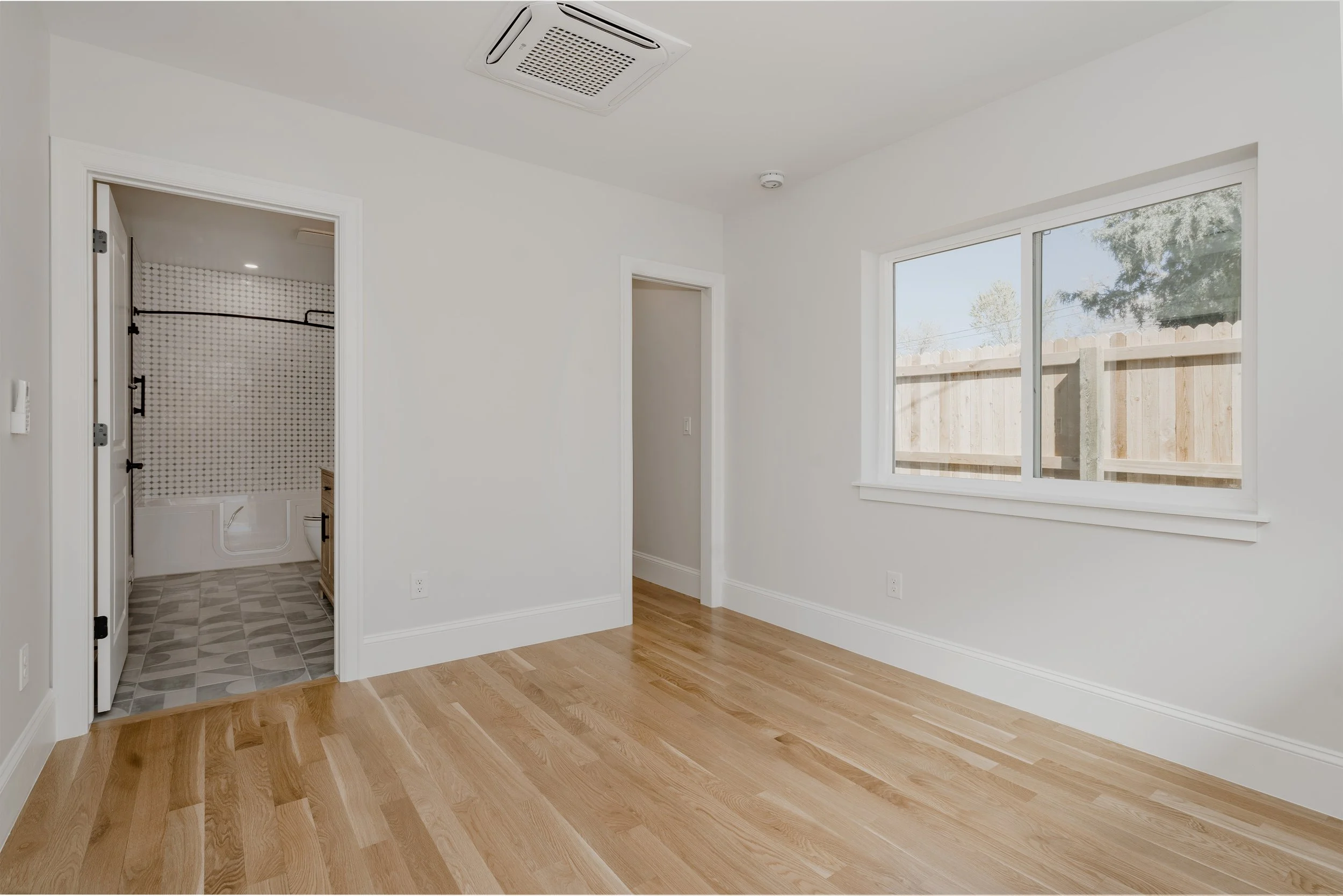 Bedroom interior of a garage-to-ADU conversion in Denver, Colorado, showing hardwood flooring, window placement, and adjacent bathroom access constructed by Prenvalley Builders.