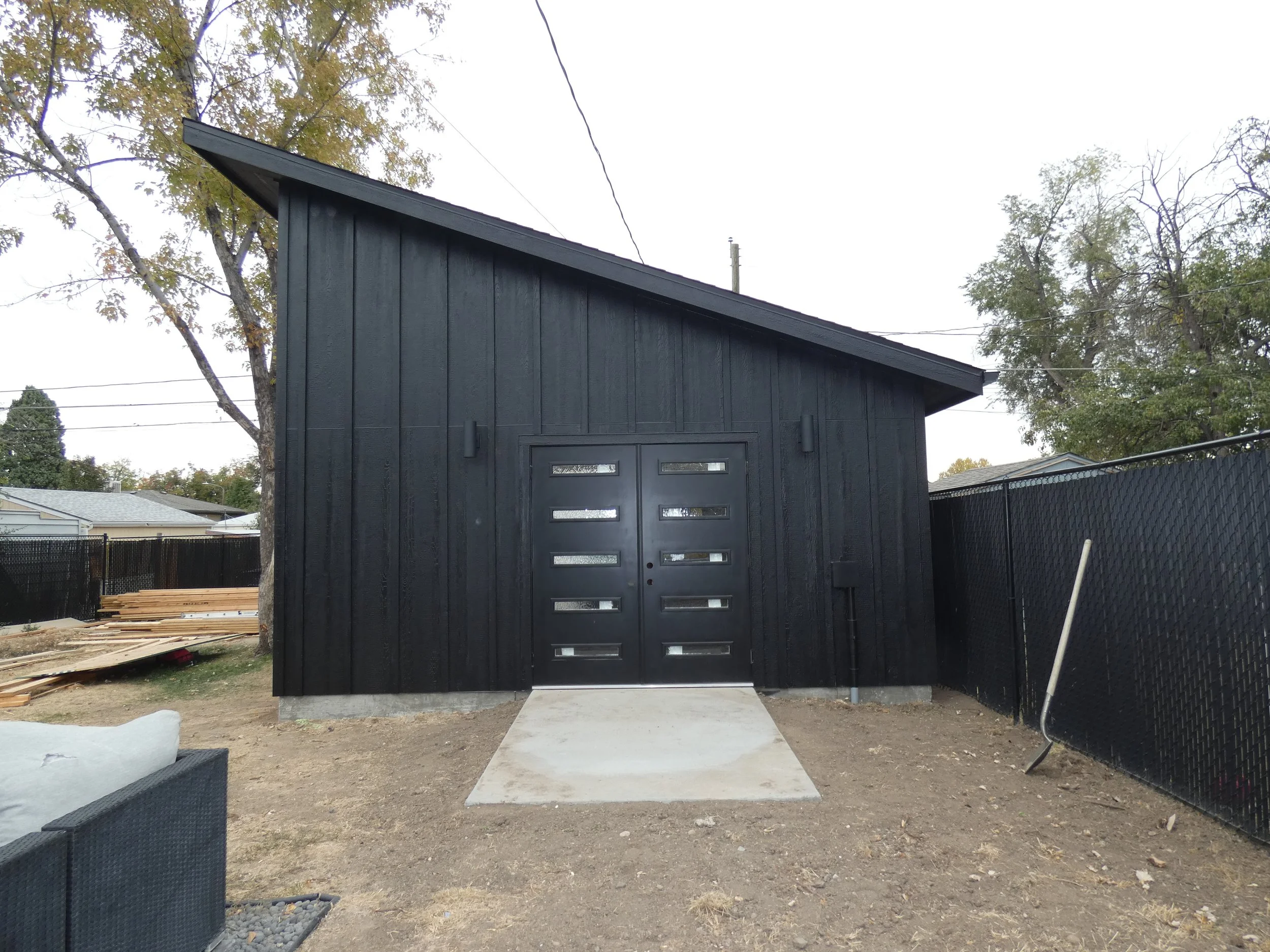 Finished front elevation of a custom detached garage in Denver’s Barnum neighborhood, featuring black vertical siding, a single-slope roof, and modern garage doors.