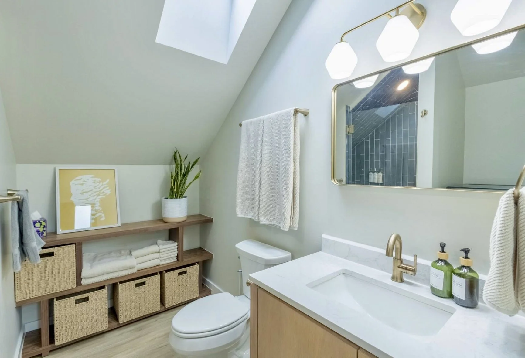 Finished bathroom interior in a custom Denver ADU featuring a skylight, sloped ceiling, modern vanity, brass fixtures, and integrated storage designed and built by Prenvalley Builders.
