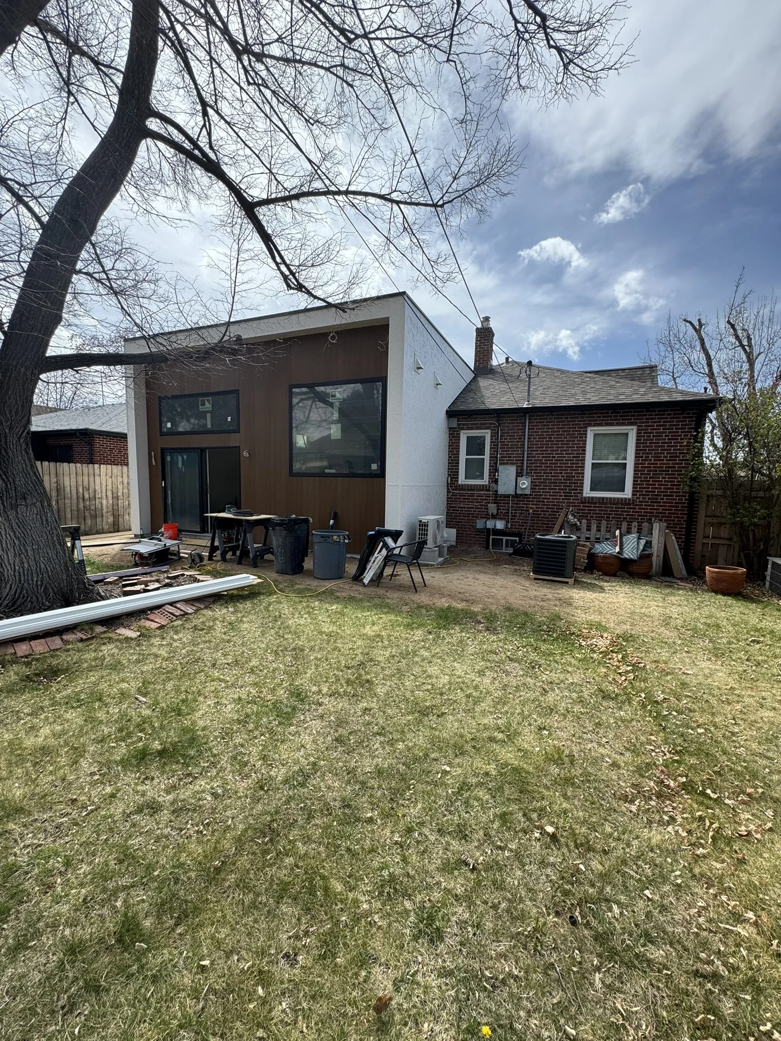 Rear view of a completed Denver home addition featuring modern stucco and wood cladding integrated with an existing historic brick Tudor home by Prenvalley Builders.