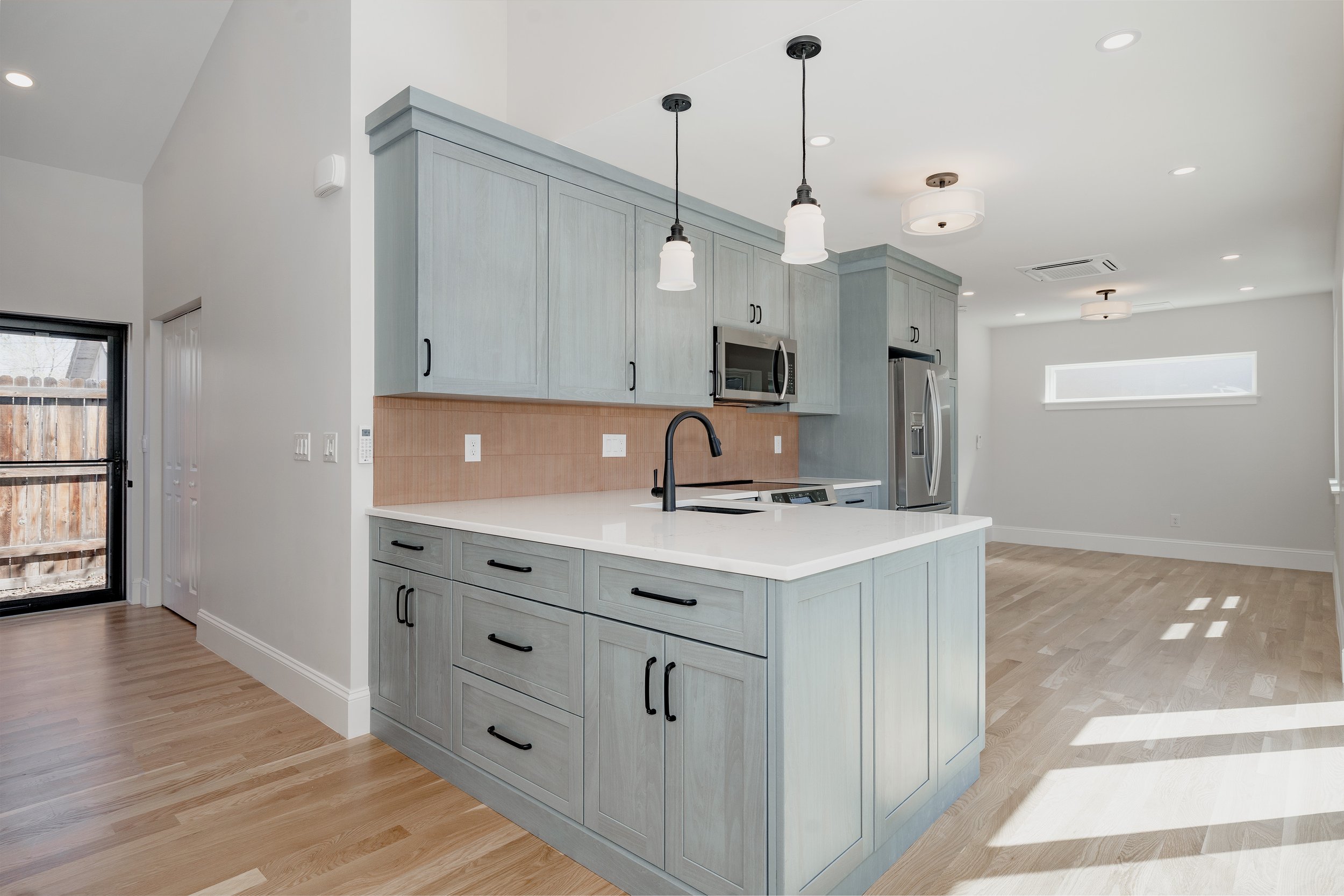 Kitchen interior of a garage-to-ADU conversion in Denver, Colorado, featuring custom cabinetry installation, quartz countertops, island seating, and integrated appliances built by Prenvalley Builders.