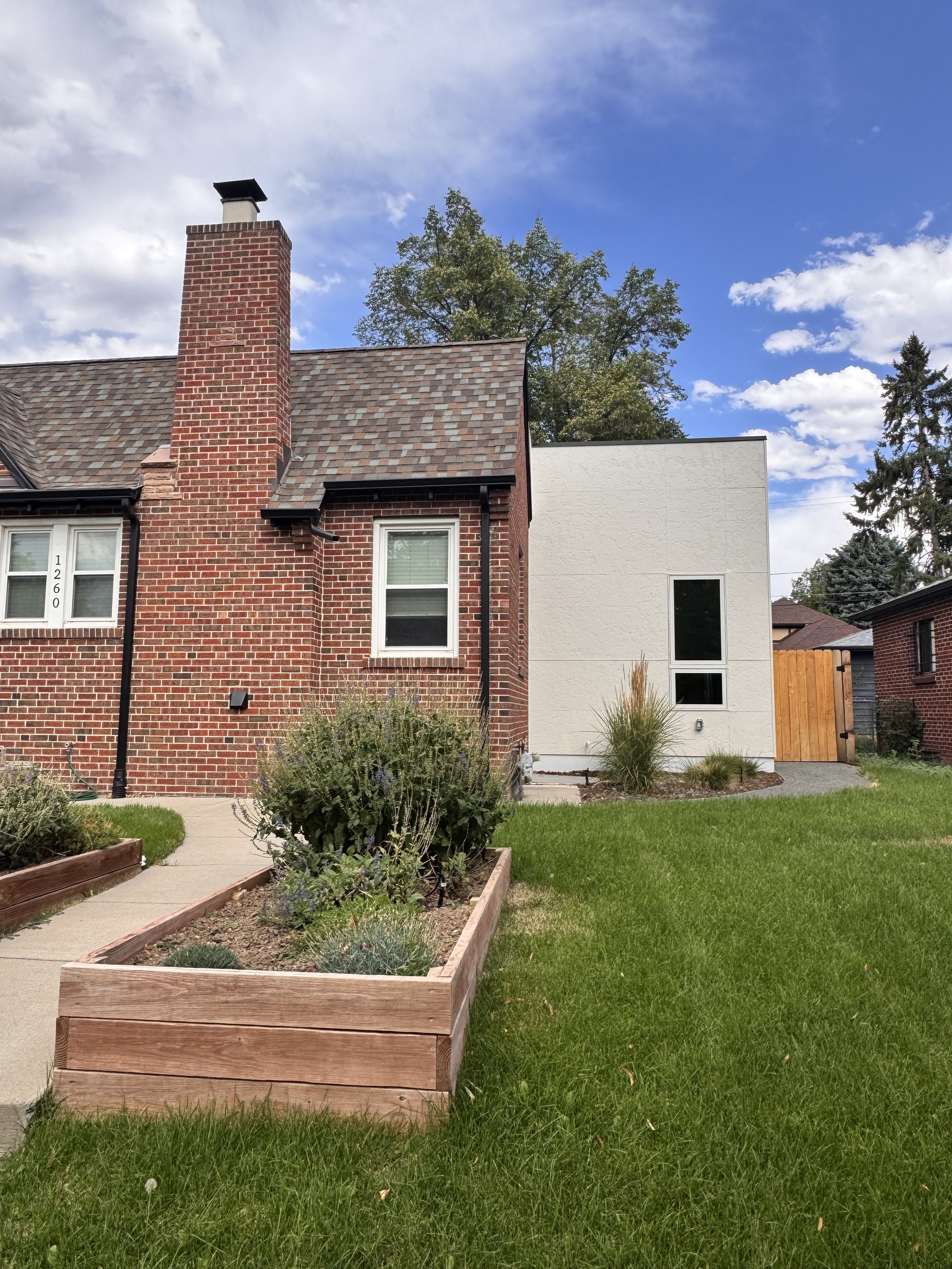Side elevation of a completed Denver home addition featuring a modern stucco exterior seamlessly connected to an existing historic brick home by Prenvalley Builders.