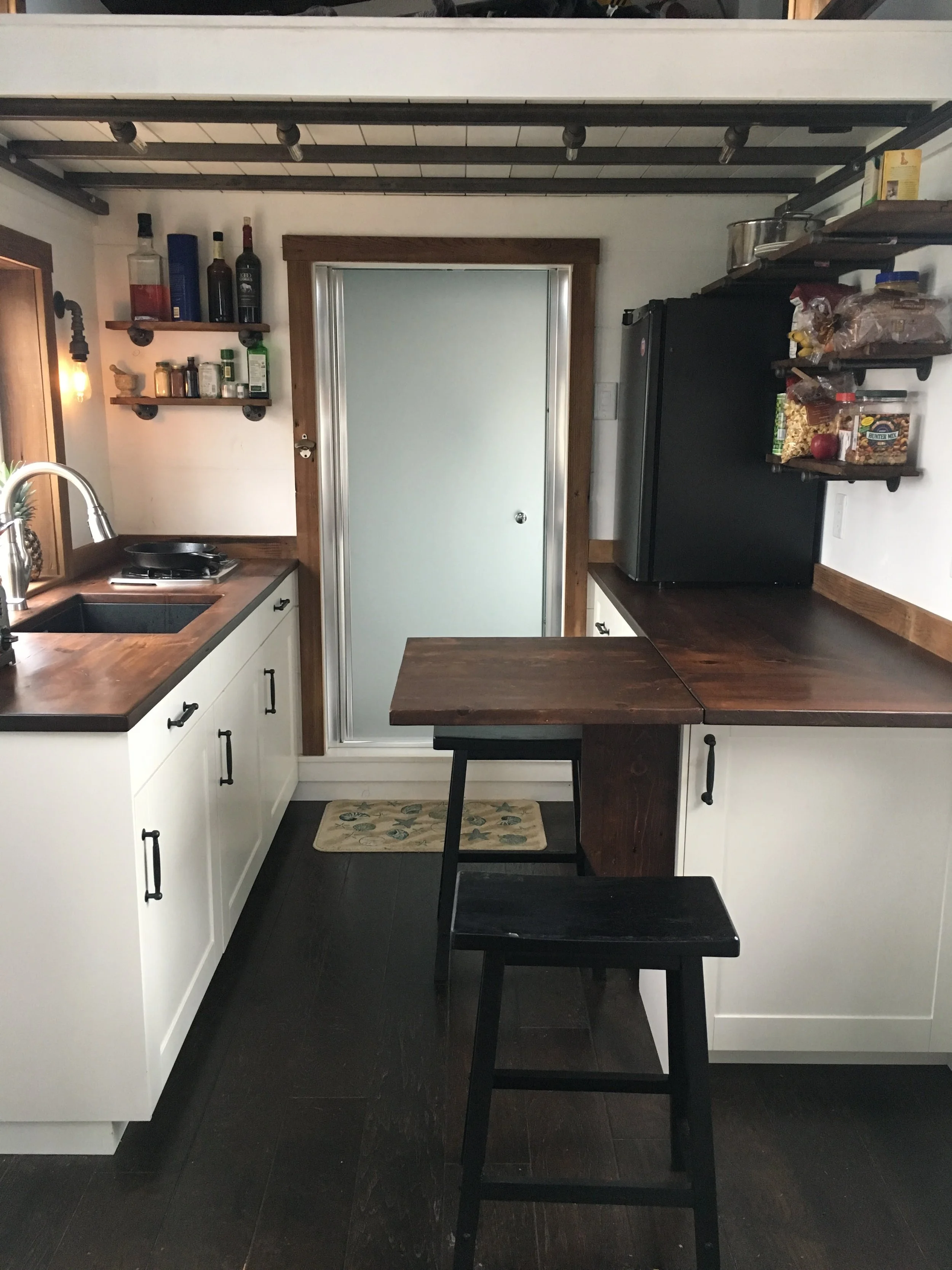 Interior kitchen of a custom mobile tiny home by Prenvalley Builders, featuring space-efficient cabinetry, wood countertops, open shelving, and integrated dining workspace.
