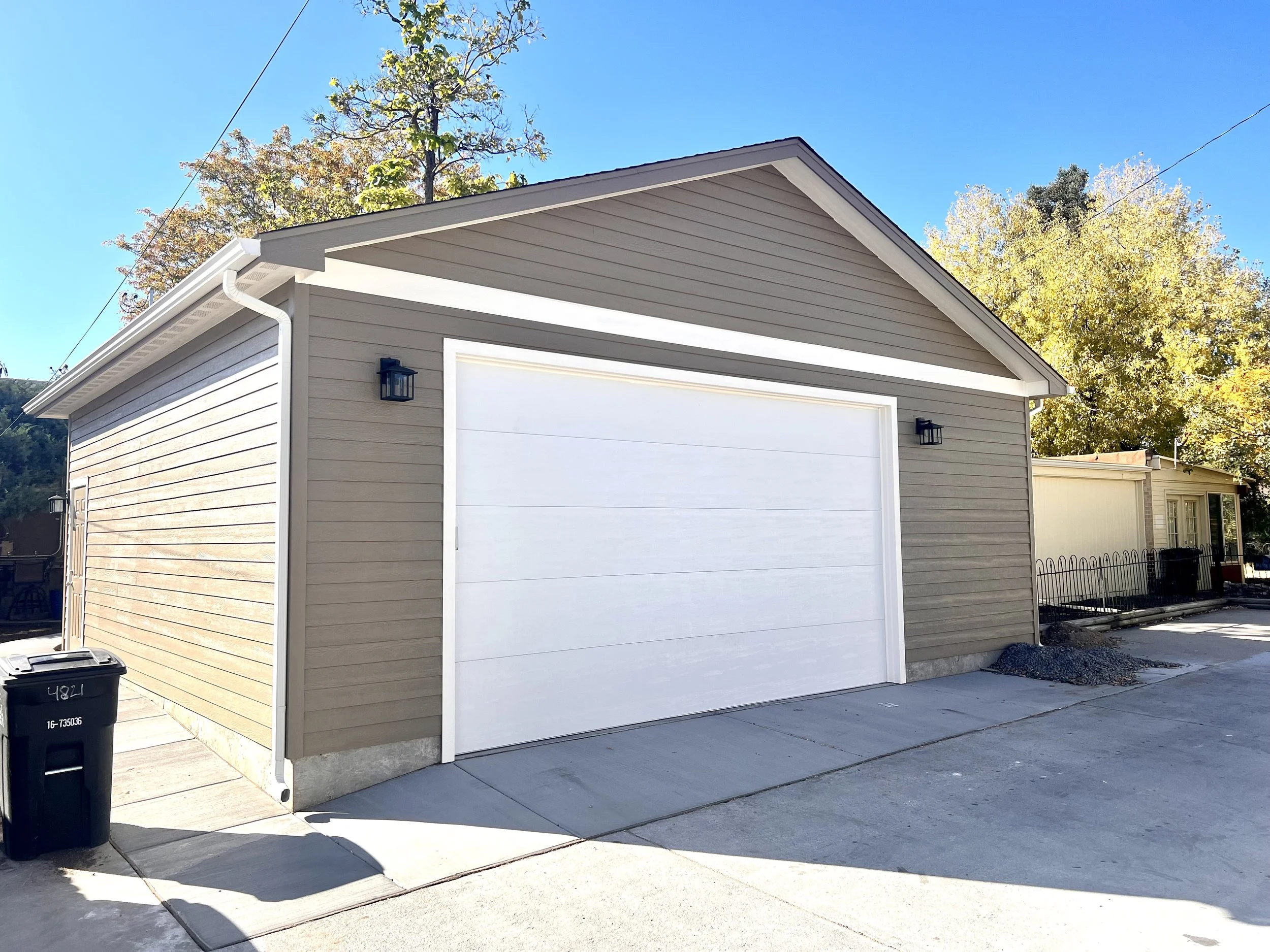 Finished custom detached garage in Denver, Colorado, featuring horizontal lap siding, a wide 2.5-car garage door, integrated exterior lighting, and a durable concrete driveway by Prenvalley Builders.