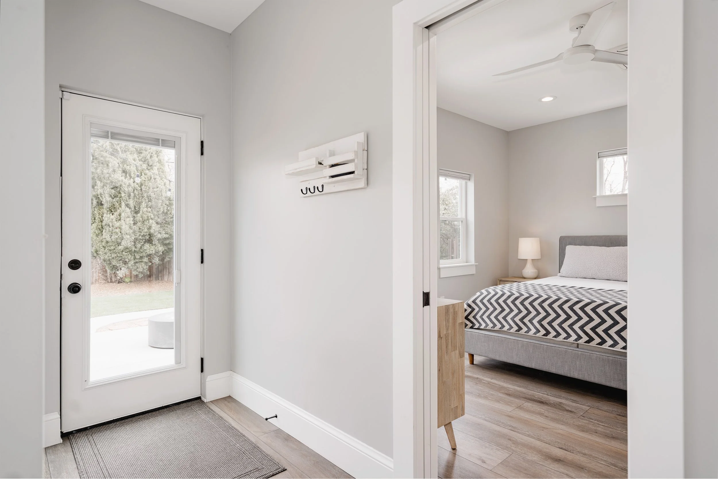 Entry view into a Denver primary-suite addition showing a bedroom with wood flooring, modern finishes, and a glass door providing direct access to the backyard.