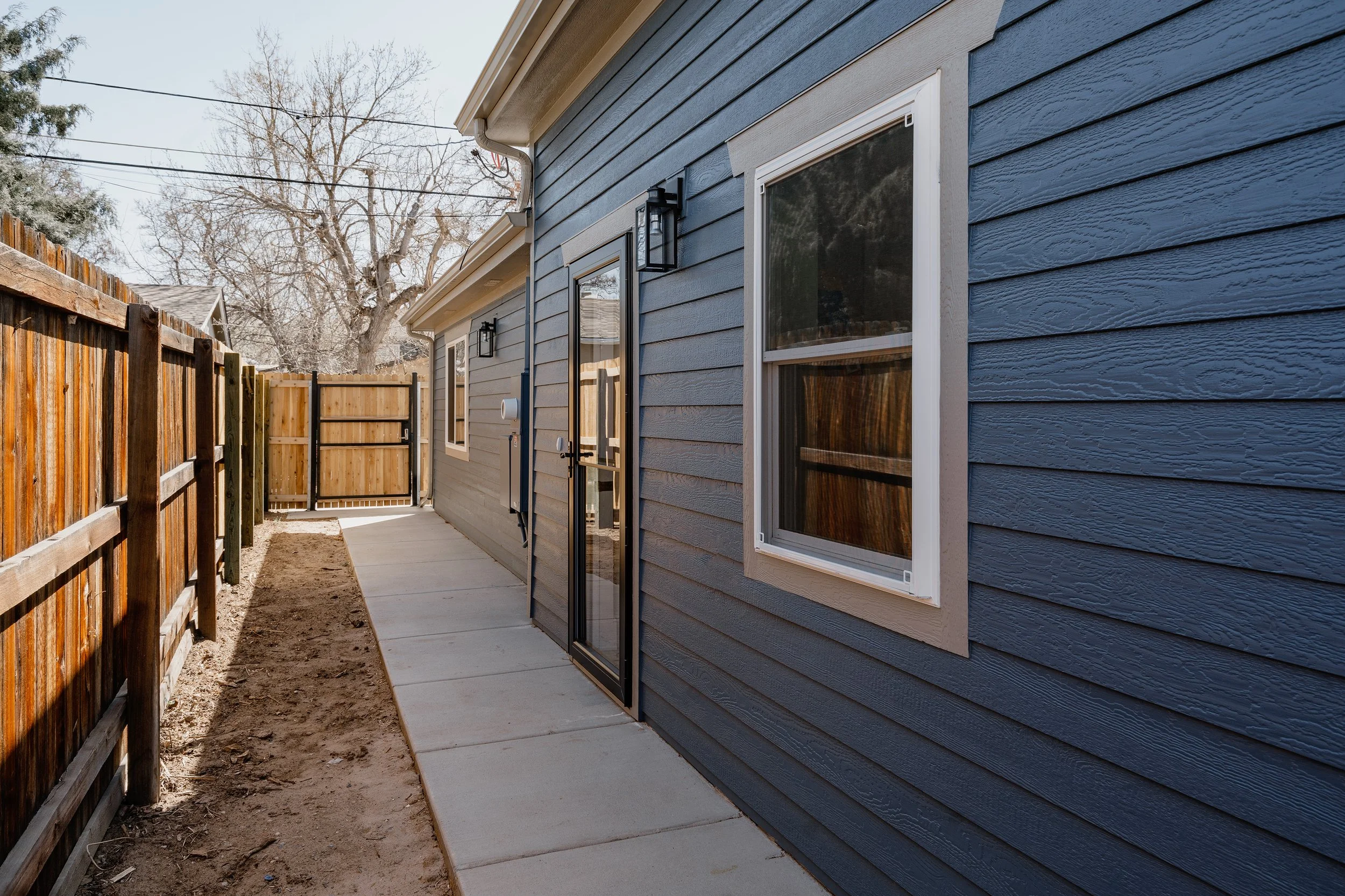 Exterior side-yard view of a completed garage ADU conversion in Denver, Colorado, featuring durable fiber cement siding, new windows, and a private entry built by Prenvalley Builders.
