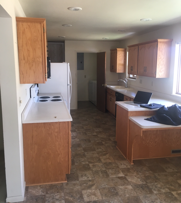 Before renovation kitchen in a Denver home with original wood cabinetry, laminate countertops, vinyl flooring, and a narrow galley-style layout prior to a full renovation by Prenvalley Builders.