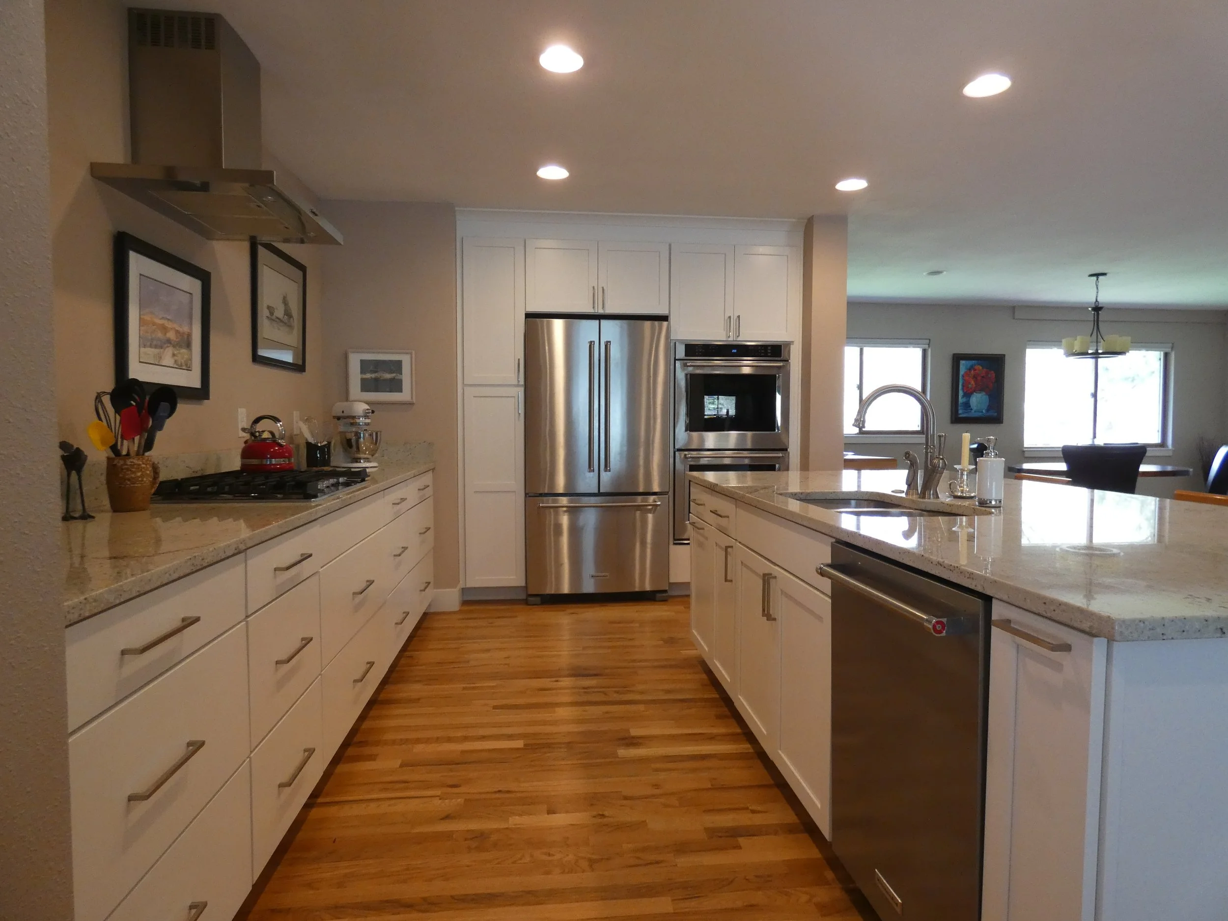 Completed kitchen after renovation in a Denver home, featuring white cabinetry, stone countertops, stainless steel appliances, and hardwood floors built by Prenvalley Builders.