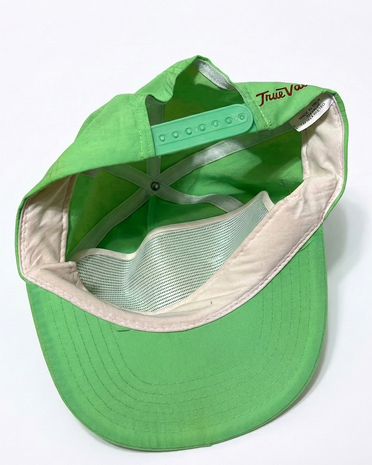 Green trucker cap turned inside out, showing interior mesh lining, adjustable strap, and tag.