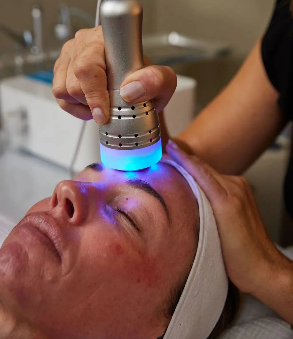 An estheticians uses a blue cold wand to soothe facial client's skin