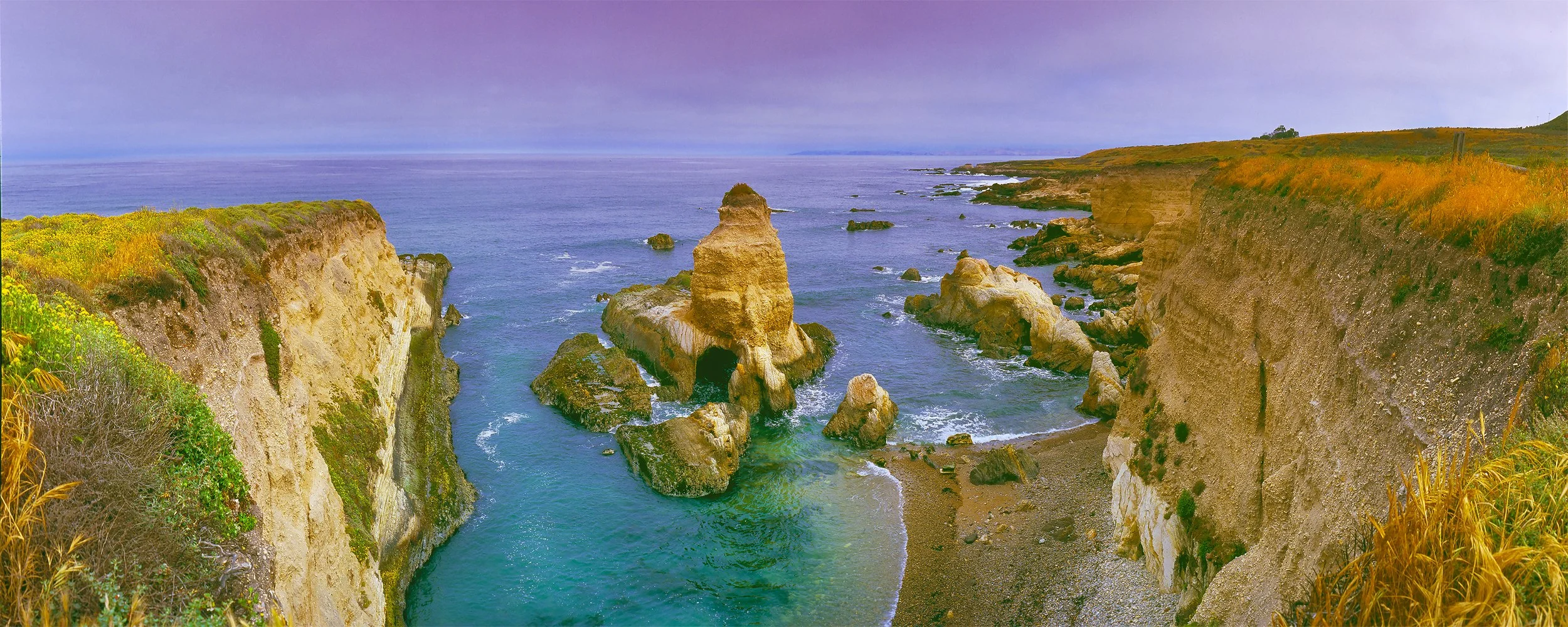 Rugged California coast cliffs and sea stacks beneath a cloudy sky.