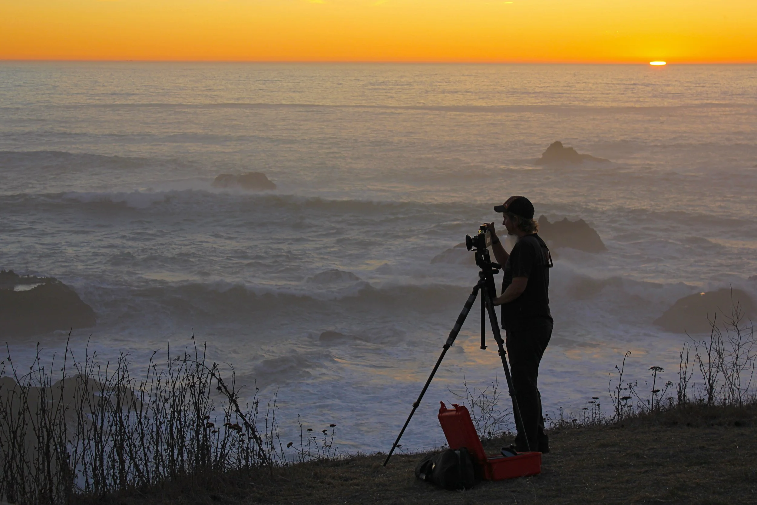 Landscape photographer Aaron Svenby using a tripod at sunset on the California coast.