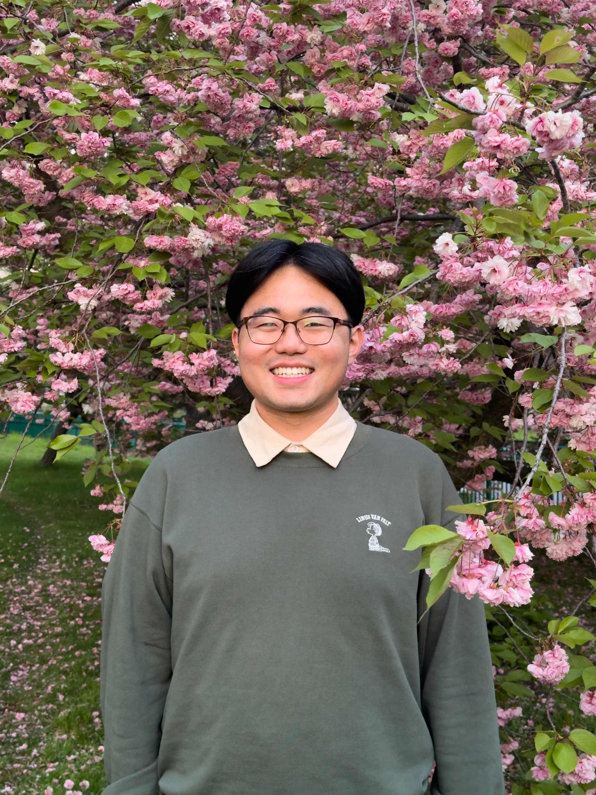 Portrait photo of Juneau Wang in front of a pink, blossoming tree.