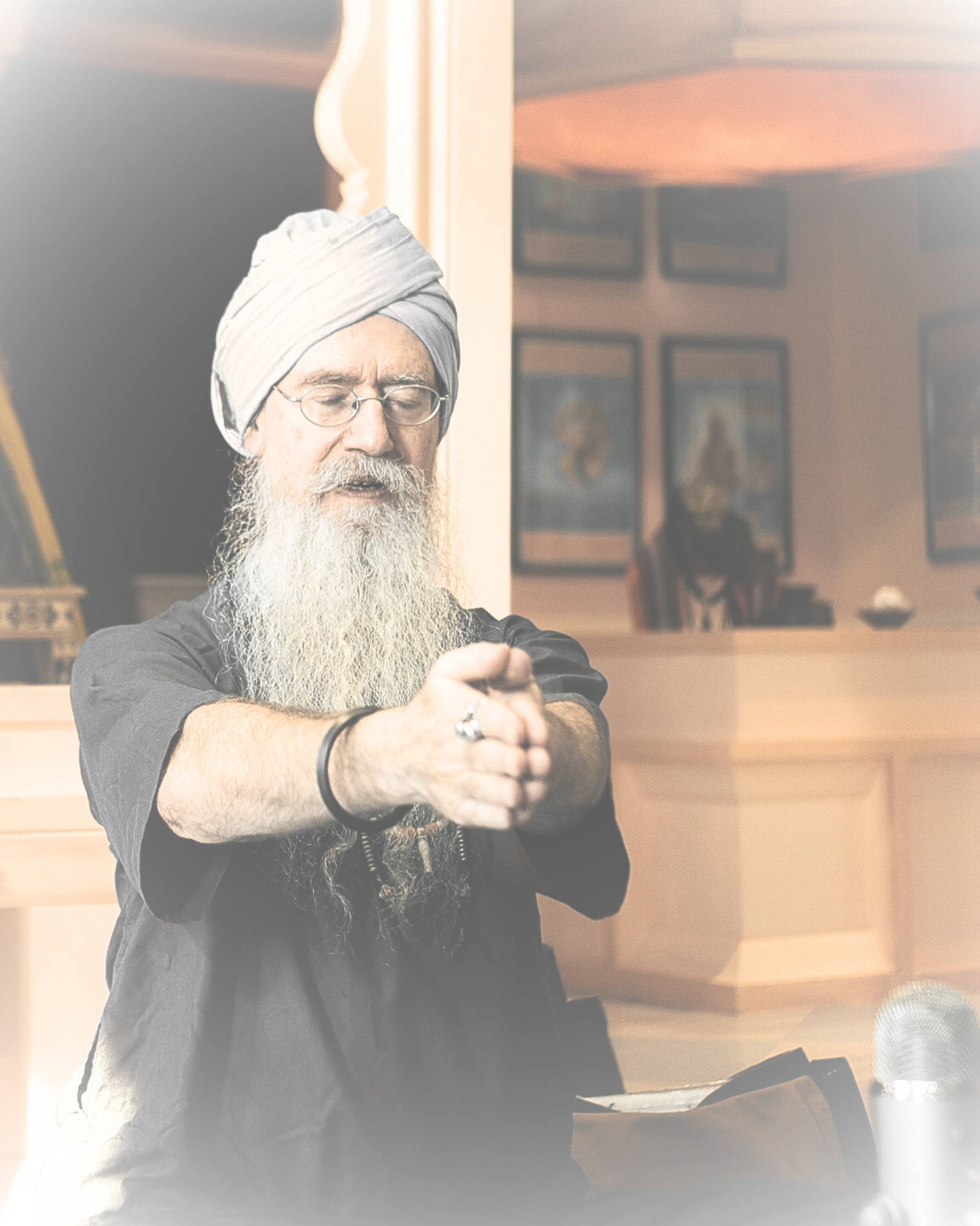 En mann med lang grå barte og tøyhodeplagg som har øyne lukket, står foran en mikrofon.