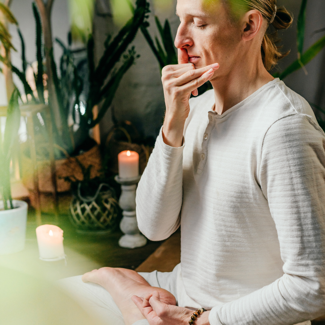 En person som mediterer i et rolig rom med grønne planter og levende lys.