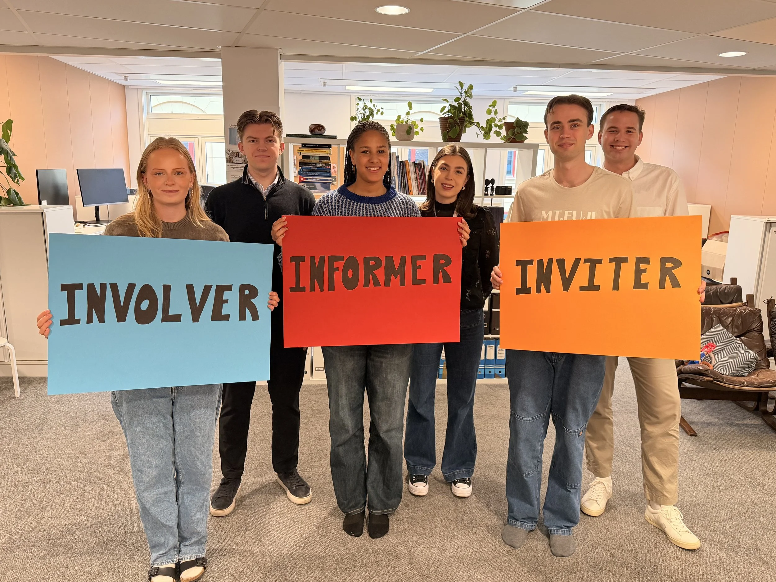 unge mennesker holder opp plakater med ordene involver, informer og inviter skrevet på
