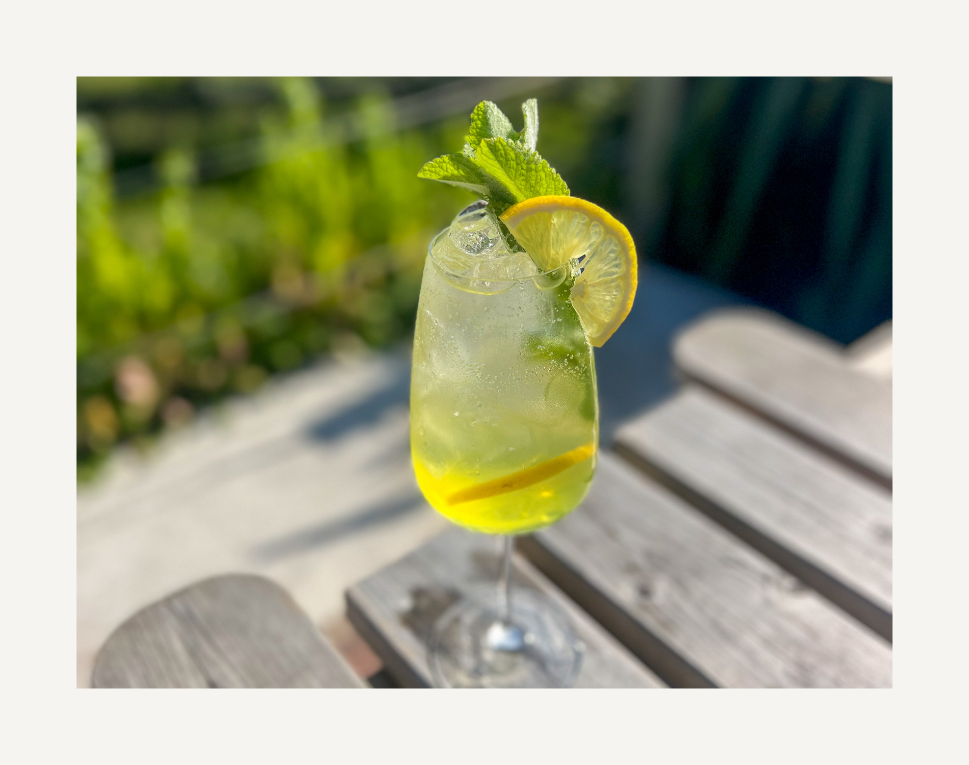 A refreshing lemon beverage with ice, garnished with lemon slices, mint leaves, and a light green liquid in a tall glass.