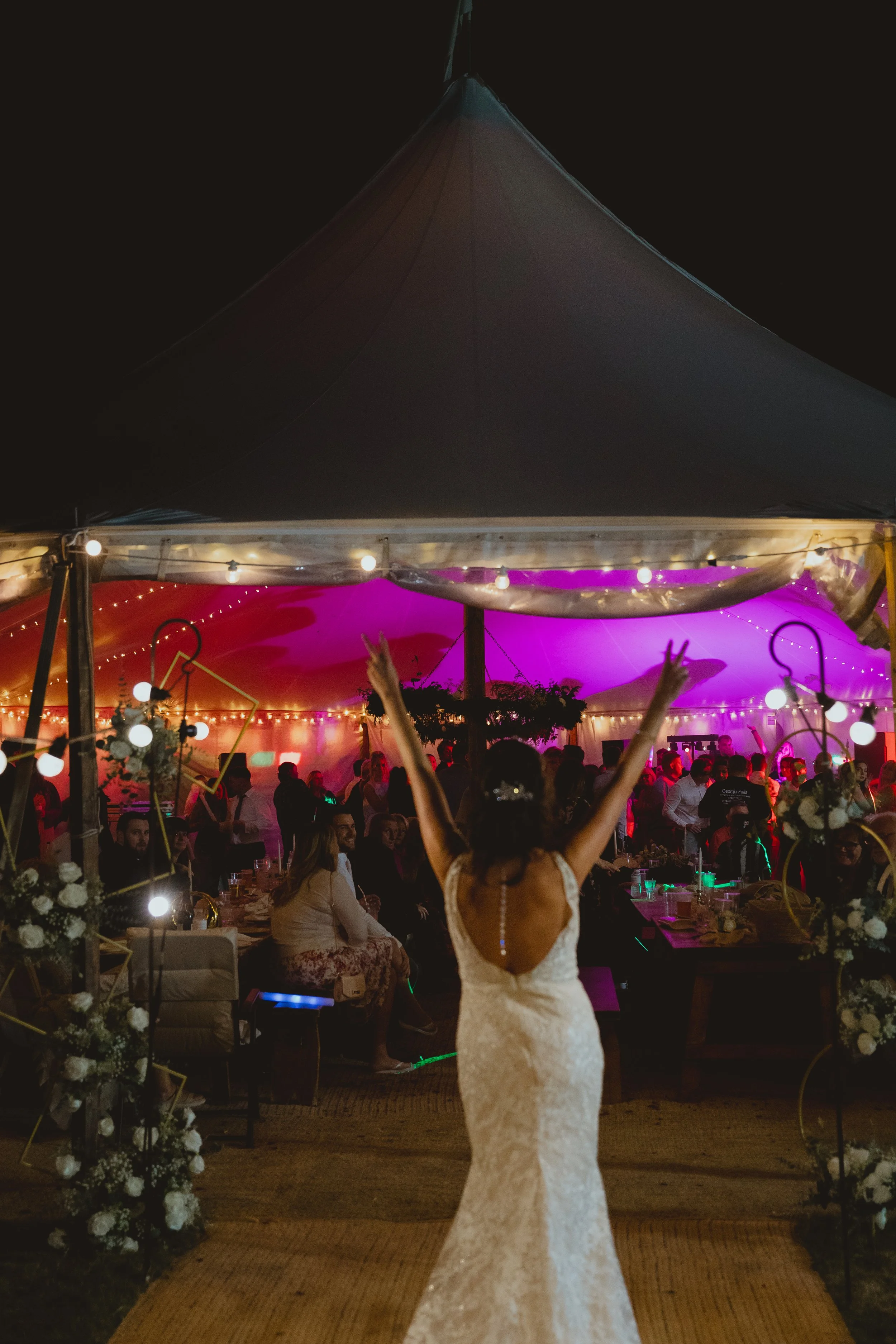 Joyful warm cinematic photograph of a bride partying with her hands in the air in front of an outdoor wedding festival marquee Lowestoft Suffolk 