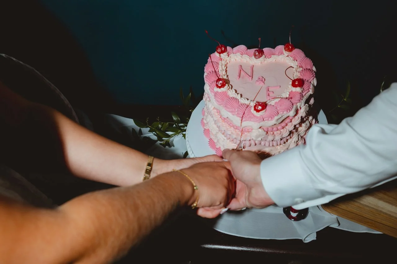 Editorial quirky flash photograph of bride and grooms hands slicing a retro throwback red pink and white layered loveheart cake with their initials on it at The Georgian Townhouse Norwich Norfolk 