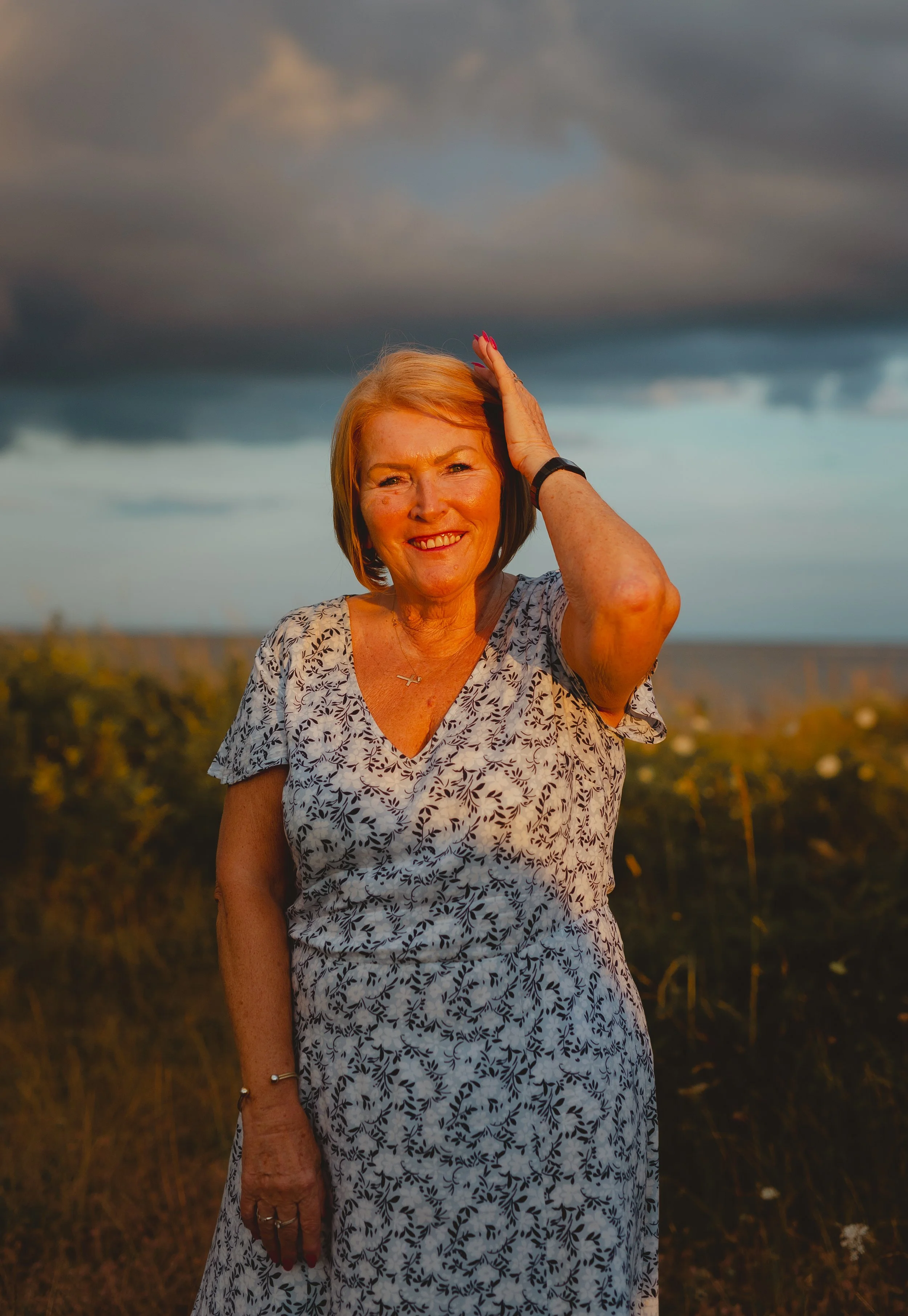 Portrait of a blonde woman putting her hand through her hair with a bright slice of sunlight shining on her with blue moody clouds in the background at Pakefield Beach Lowestoft Suffolk 