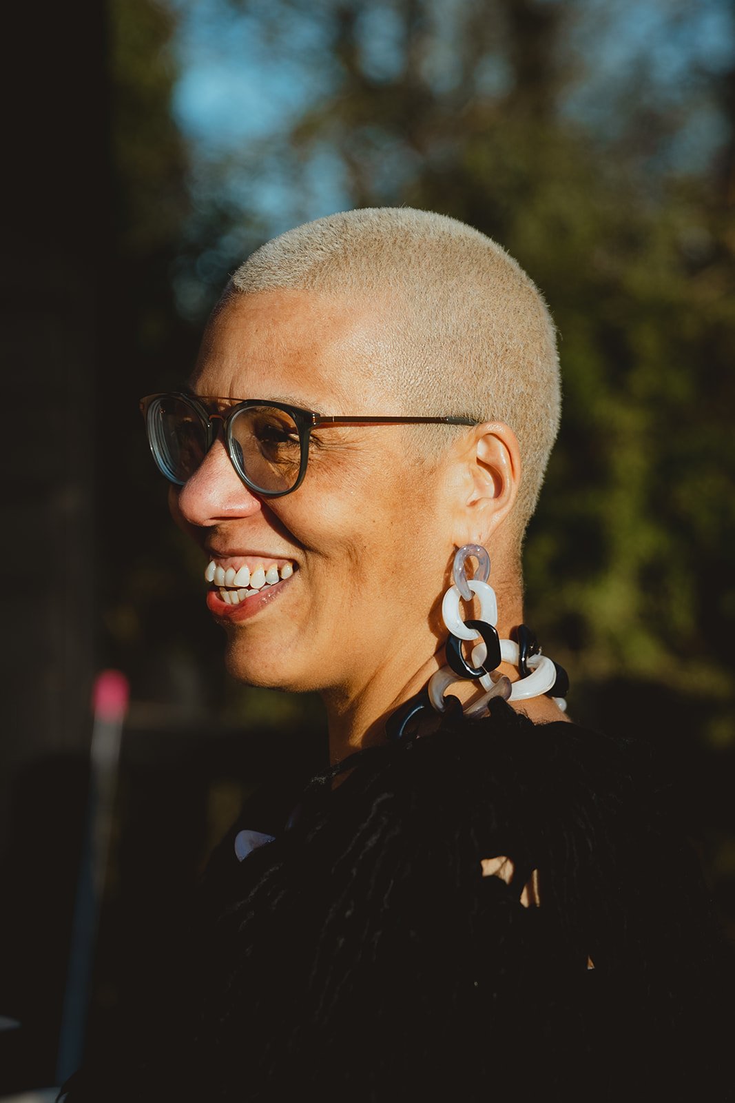 Bright highly contrasted documentary image of smiling creative black woman with a blonde buzzcut and large earrings at sunset at Restaries Halesworth Suffolk 
