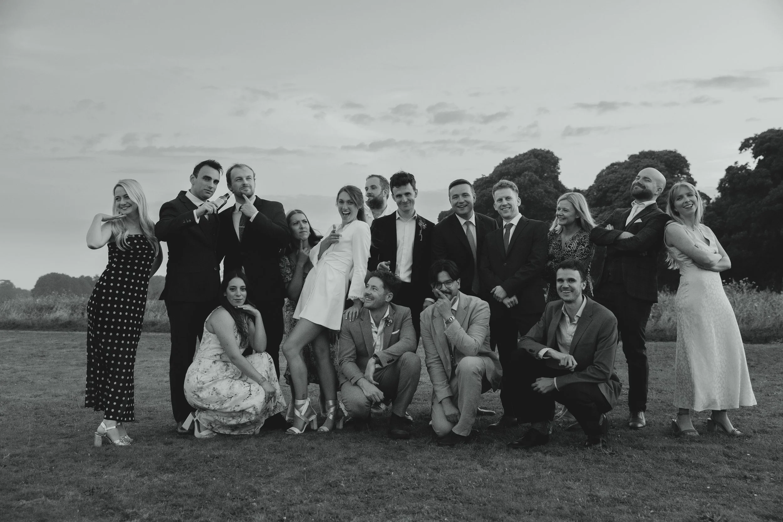 Editorial wedding guest party photo in black and white of bride in minidress making a funny pose and friends posed around her Sudbourne Hall Orford Suffolk Coast 