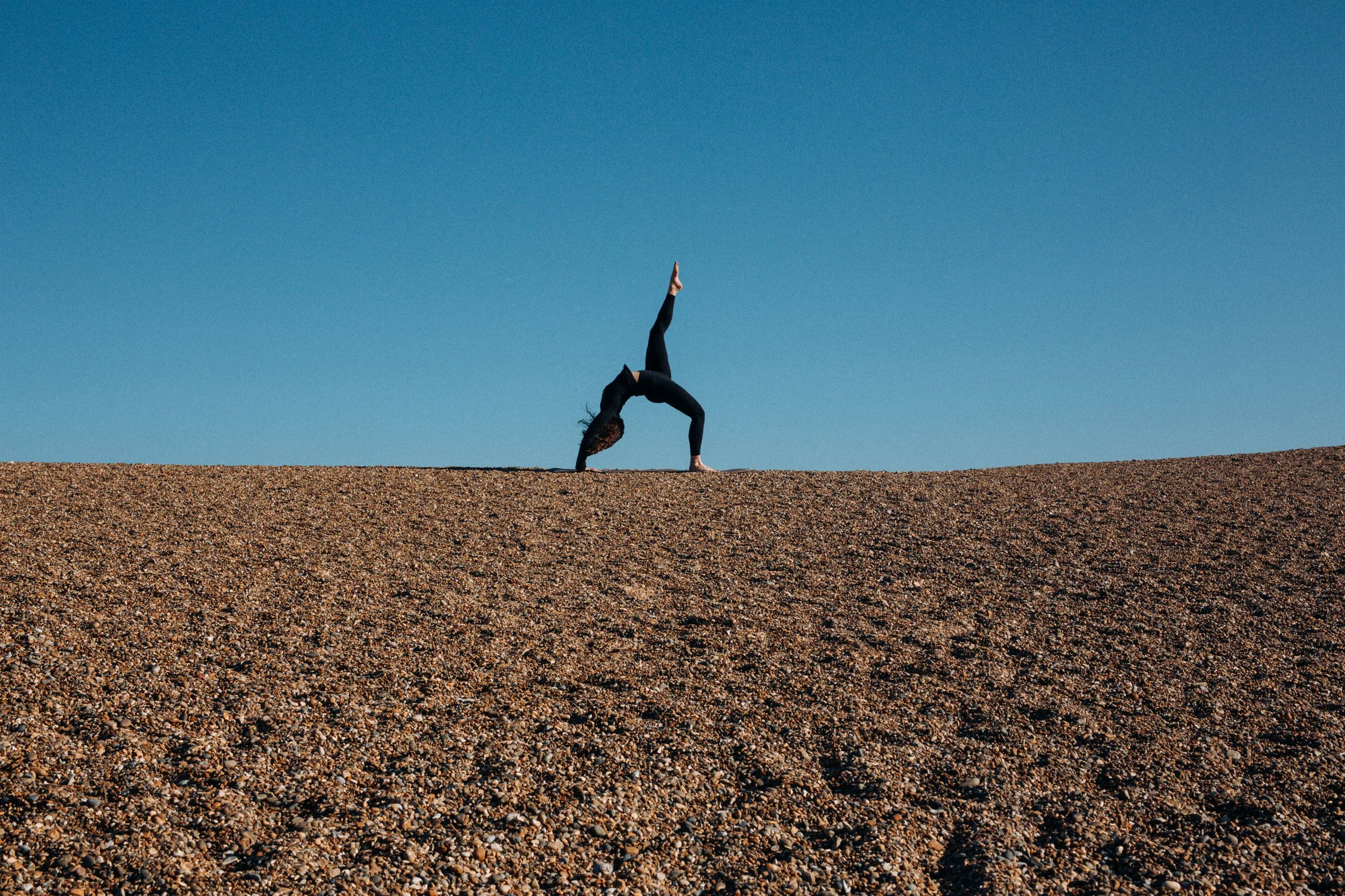 Cinematic wide shot of a yoga teacher doing a pose in the middle of the beach in Dunwich Suffolk Coast 