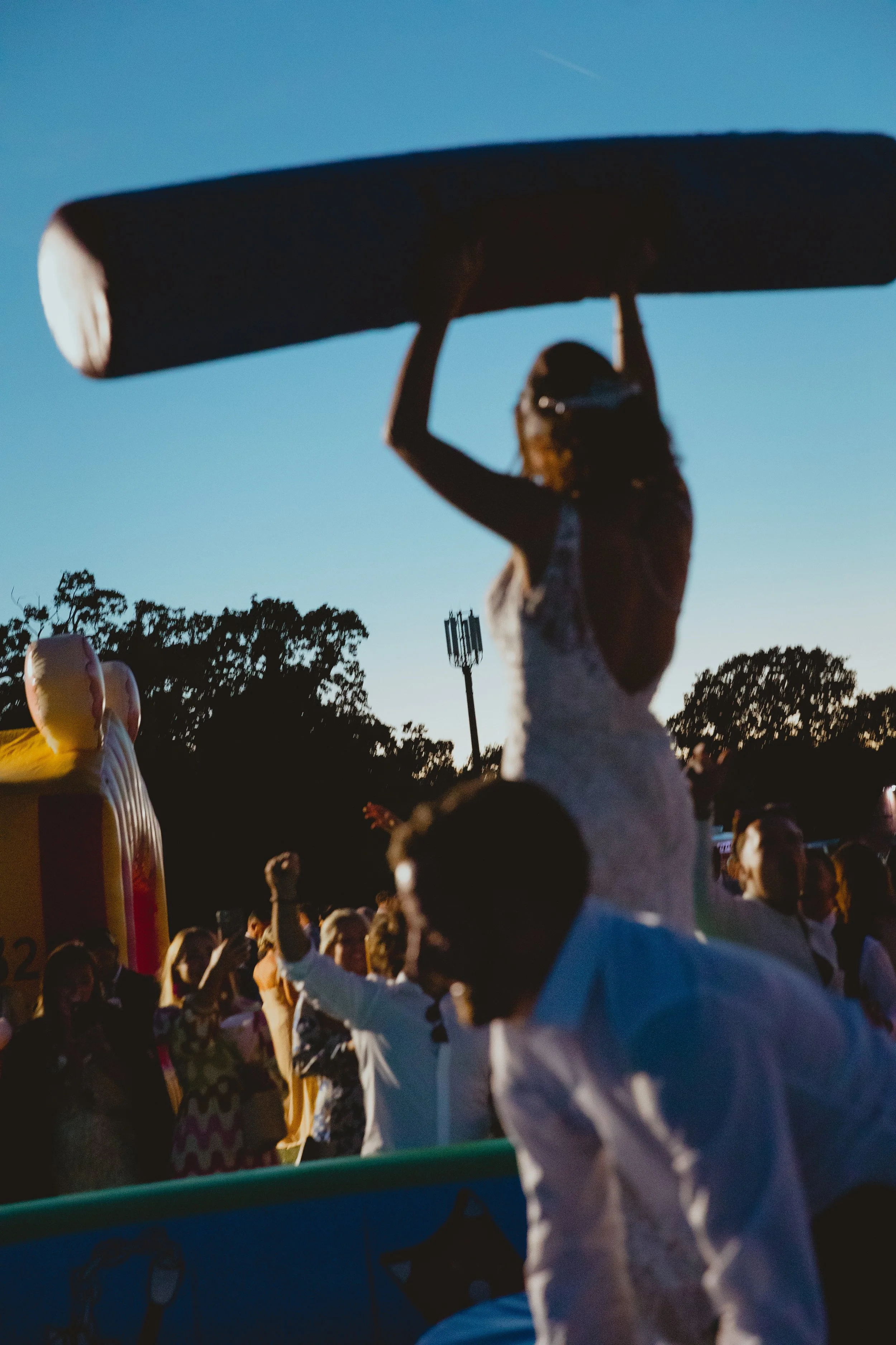 fun bride and groom lifting inflatable wrestling apparatus to the sky at twilight in suffolk  
