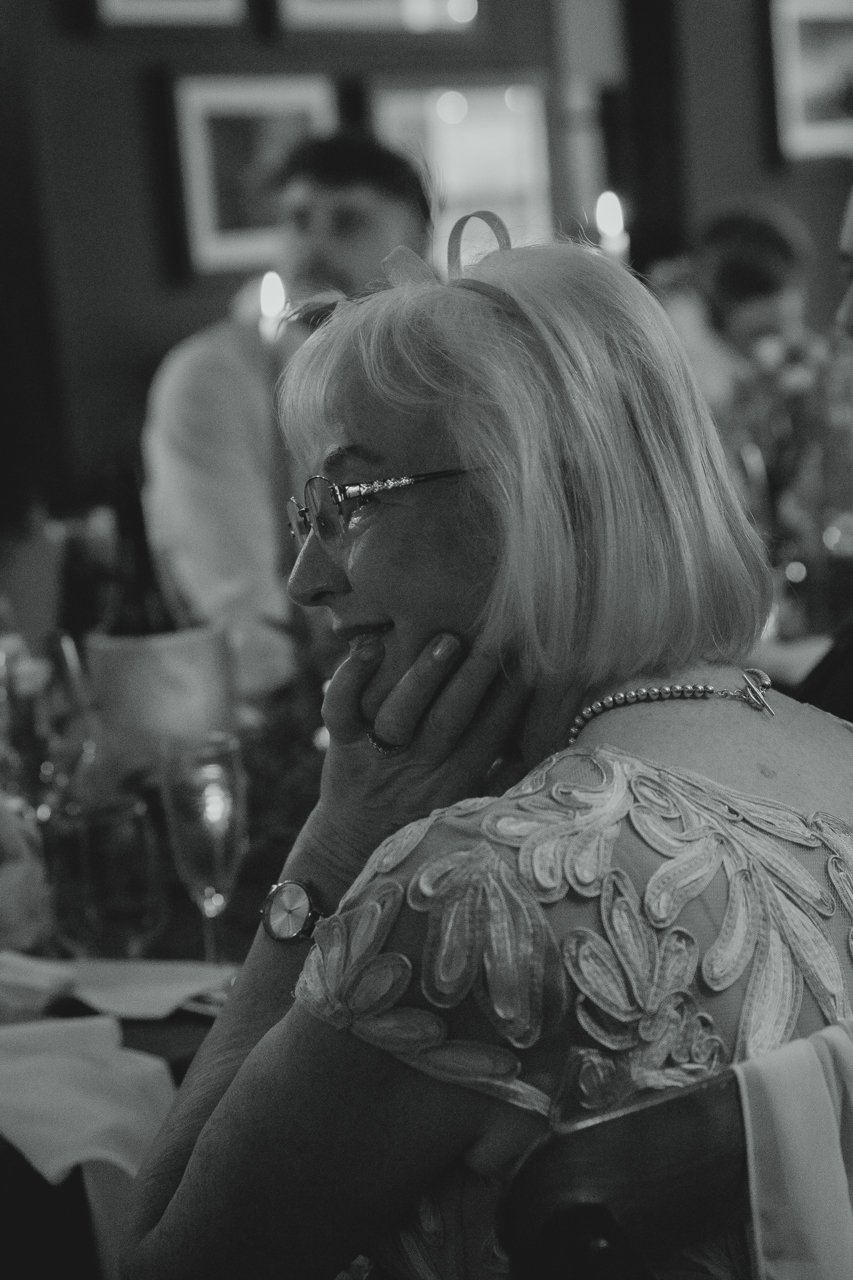 Black and white photograph of mother of bride warmly smiling indoors lit by candlelight at speeches at Georgian Townhouse Norwich Norfolk 