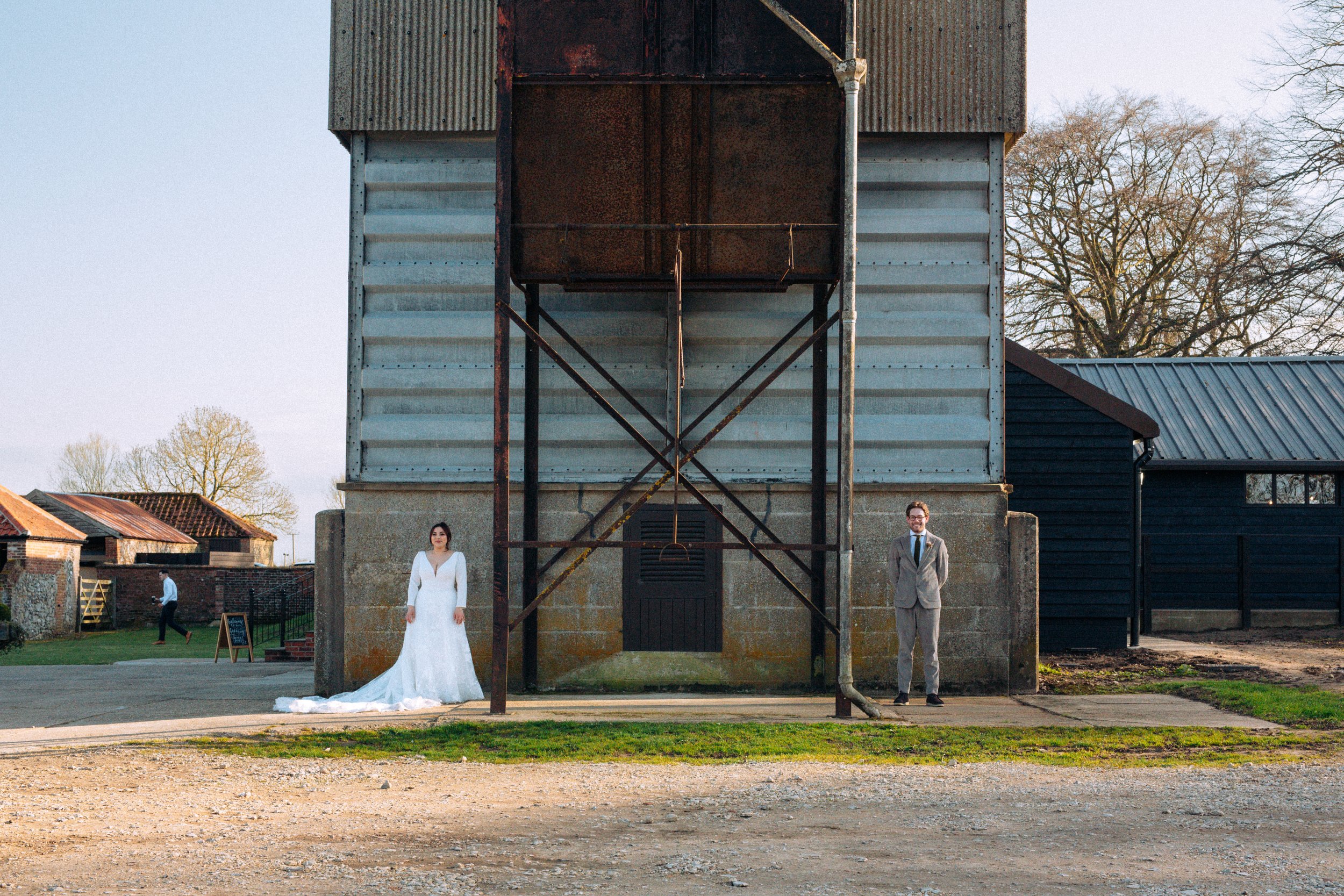 Editorial landscape photo of bride and groom far apart staring out into the distance against industrial metal backdrop of Curds Barn Norfolk Norwich 