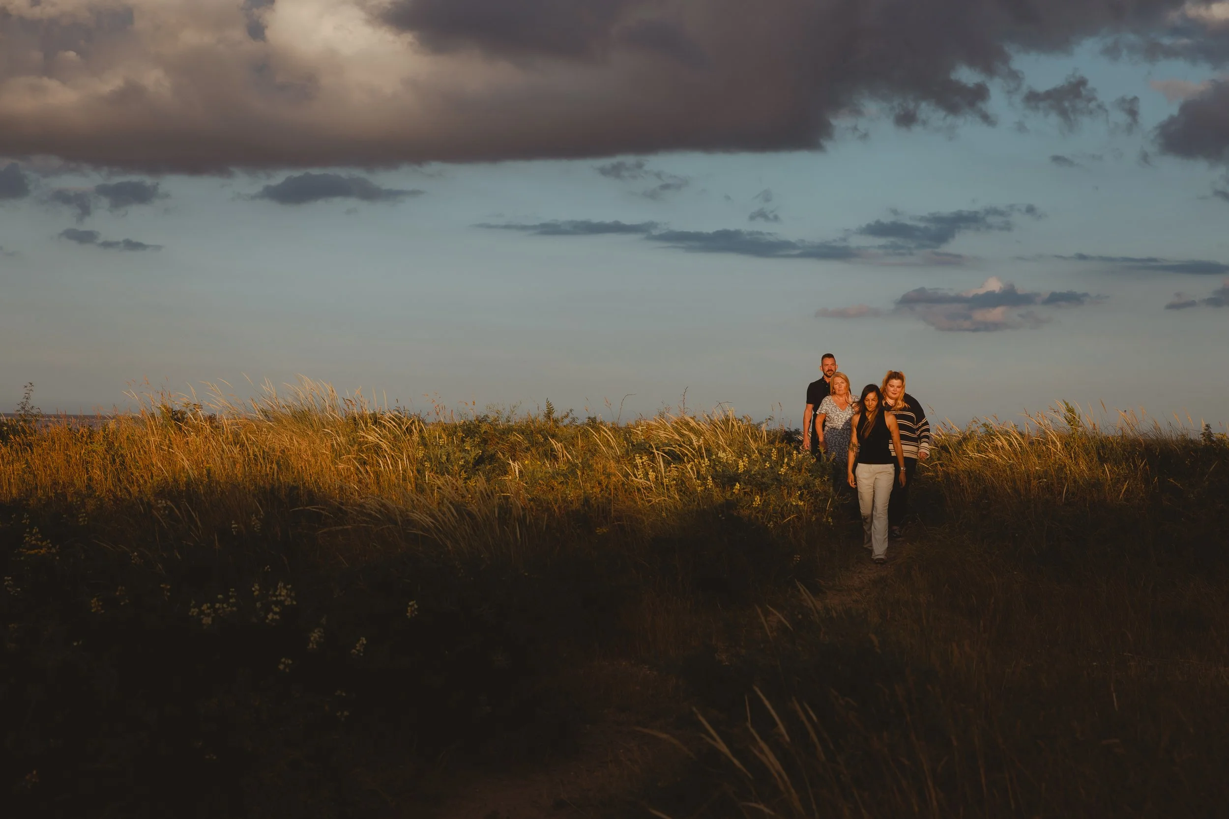 Group of people walking across dunes sunlit by a strip of light at Pakefield Suffolk Lowestoft with inky blue sunset behind them
