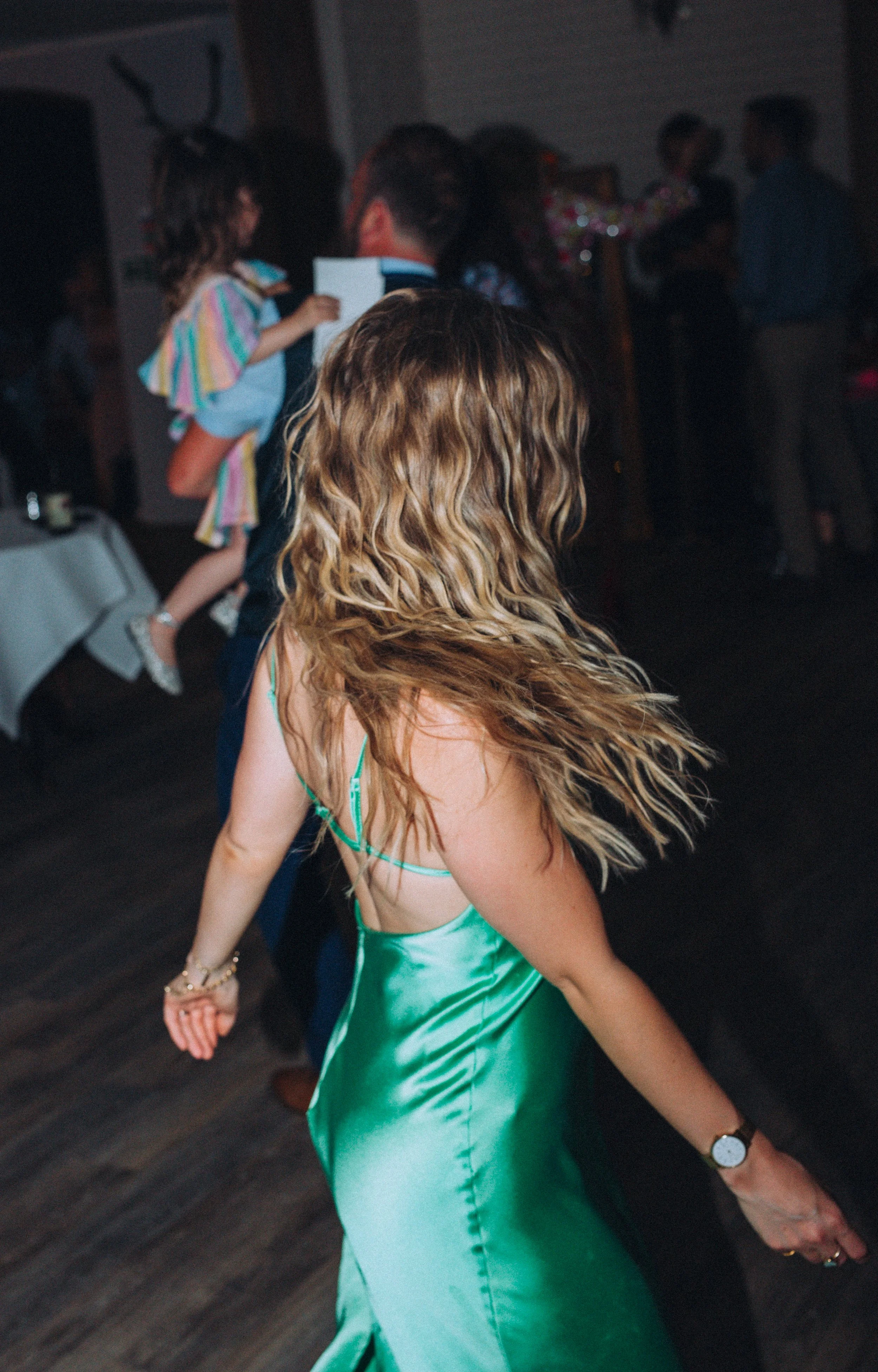 Editorial flash evening dancing shot of woman in motion with wavy hair and green dress on dancefloor  