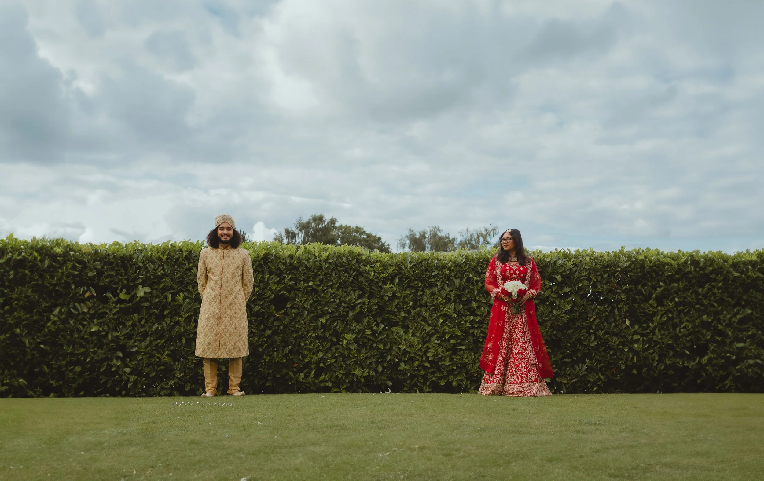 wide editorial couple shot of south Asian mixed race couple against green topiary and a big blue sky at Wensum lodge gold and spa in Norwich Norfolk 