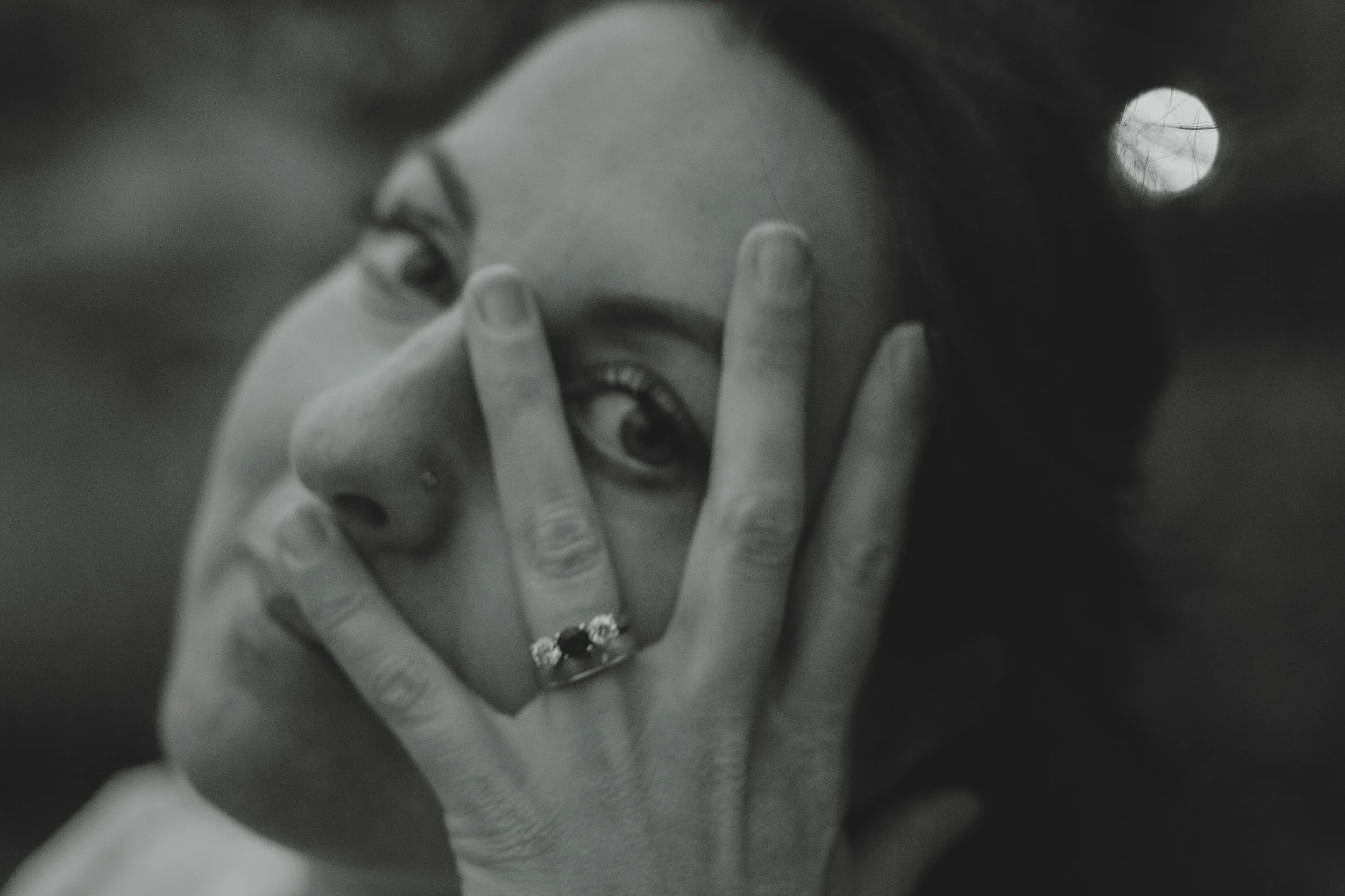 Black and white soft close up portrait of a dark haired holistic woman looking through two fingers at the camera in Somerleyton Suffolk 