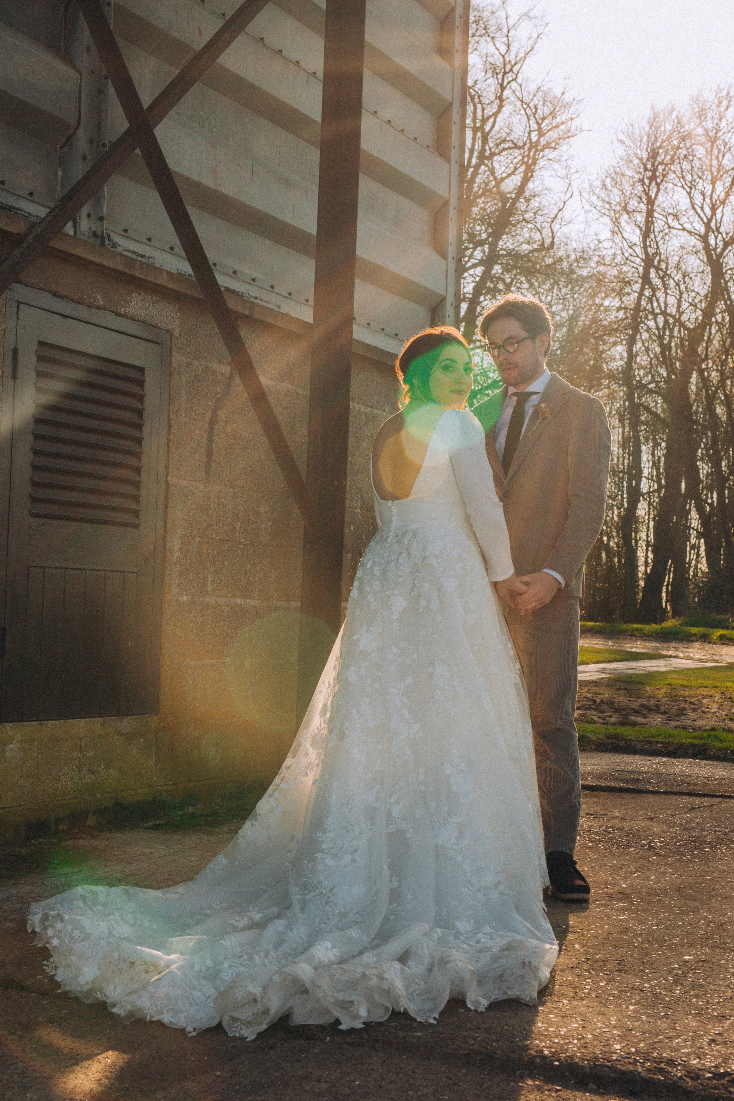 Backlit romantic couple photograph of bride and groom holding hands against an editorial industrial backdrop at Curds Barn Norfolk Norwich 