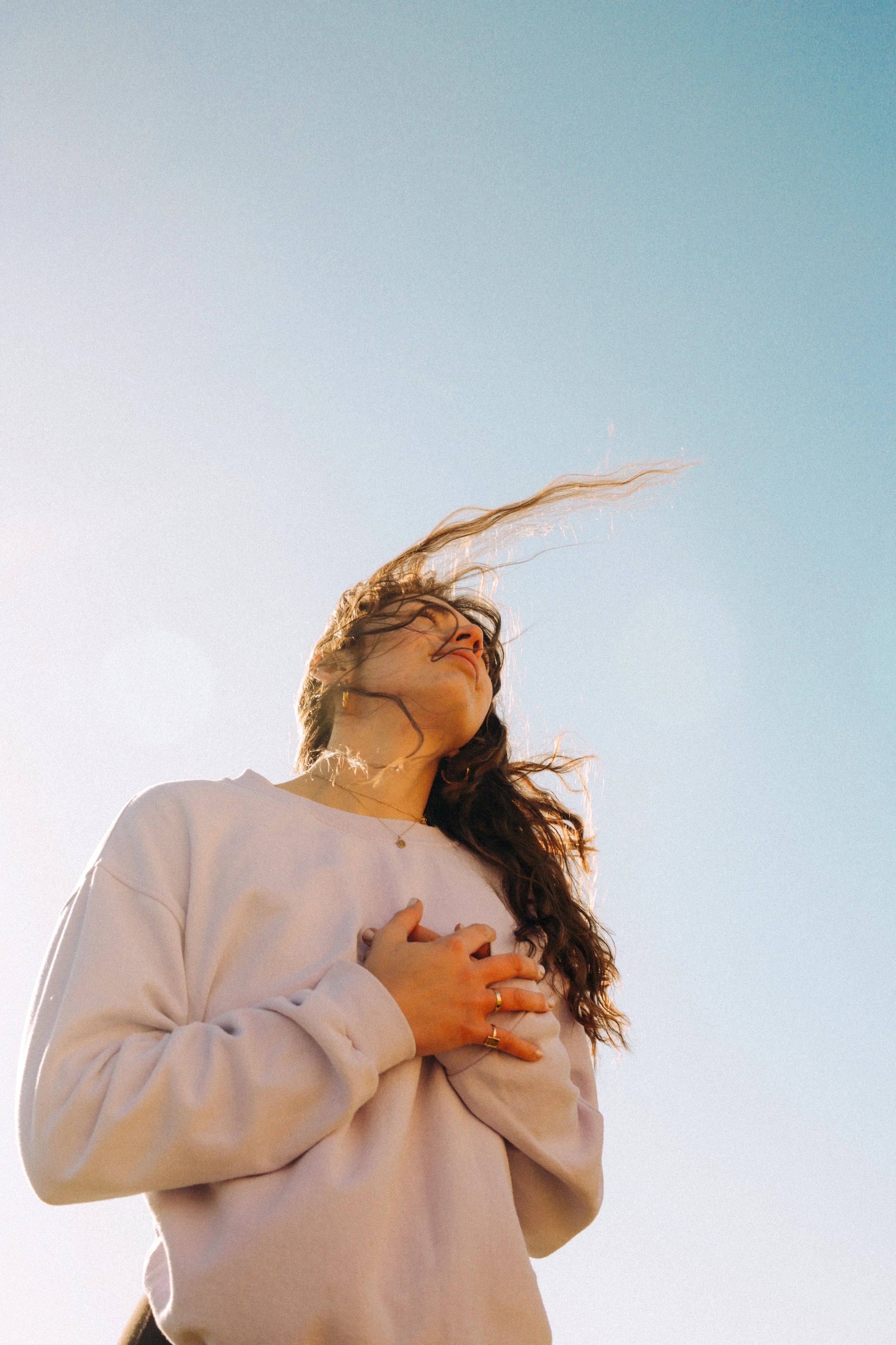Bright blue portrait of a yoga woman against the sky with wavy dark hair looking up with her hand on her heart in Dunwich Suffolk Coast  