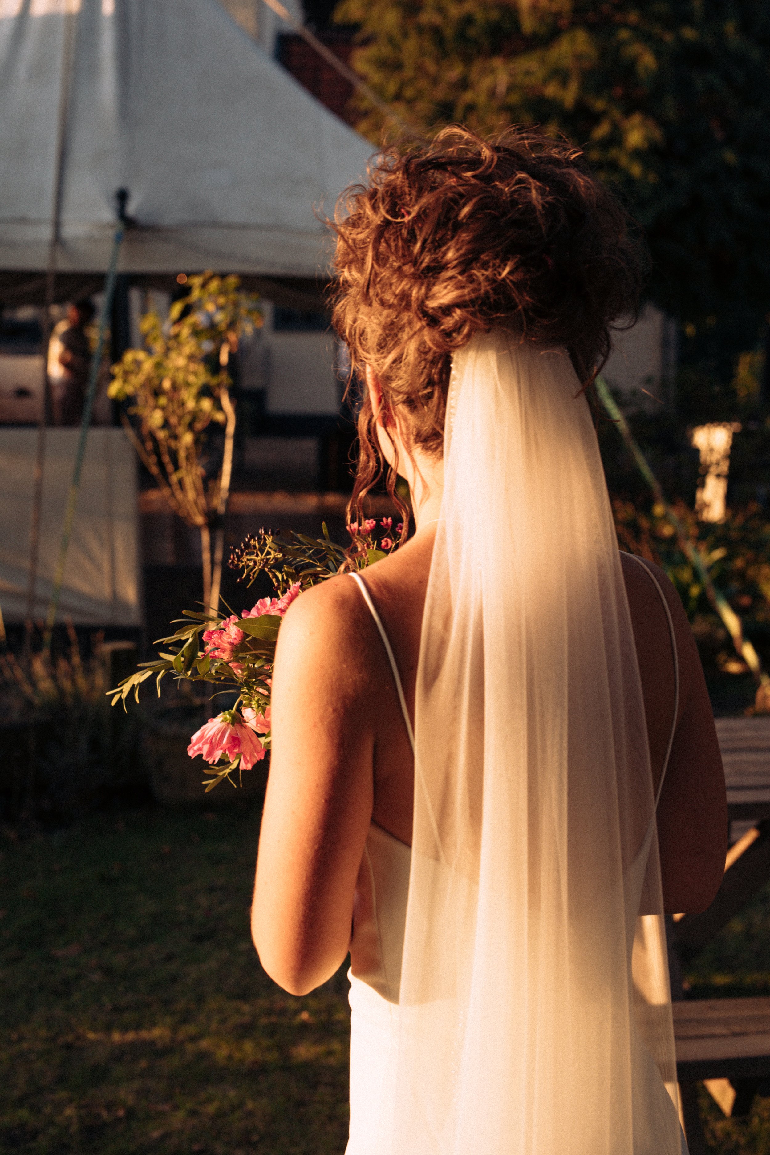Golden hour portraits of bride with the sun illuminating her veil take from the back as she looks out onto a marquee at Wheatacre White Lion Beccles Suffolk 