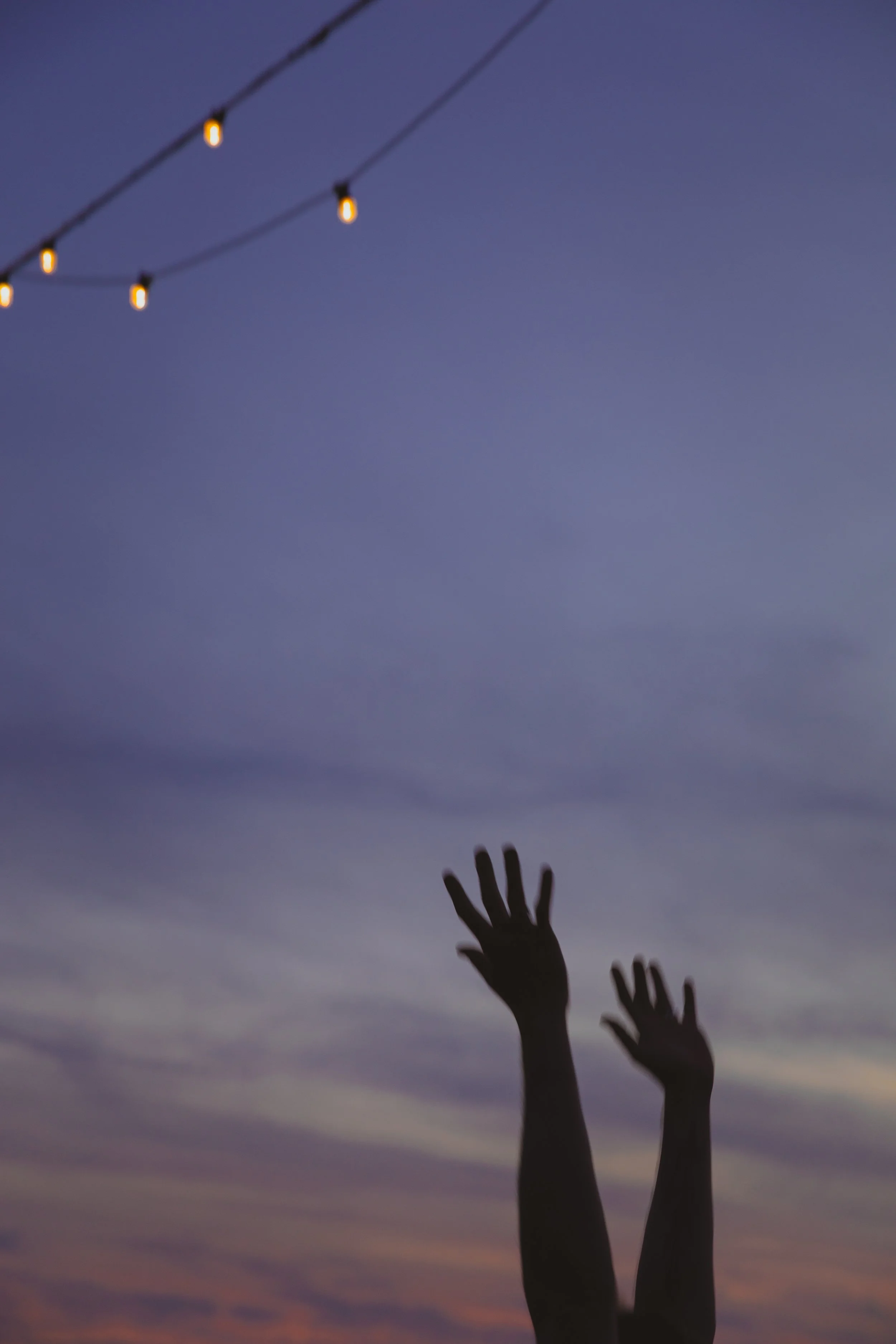 Twilight photography of two hands silhouetted against the sky with festoon lights in the foreground against a purple and pink sky in Oulton Broad Suffolk Broads Norfolk 