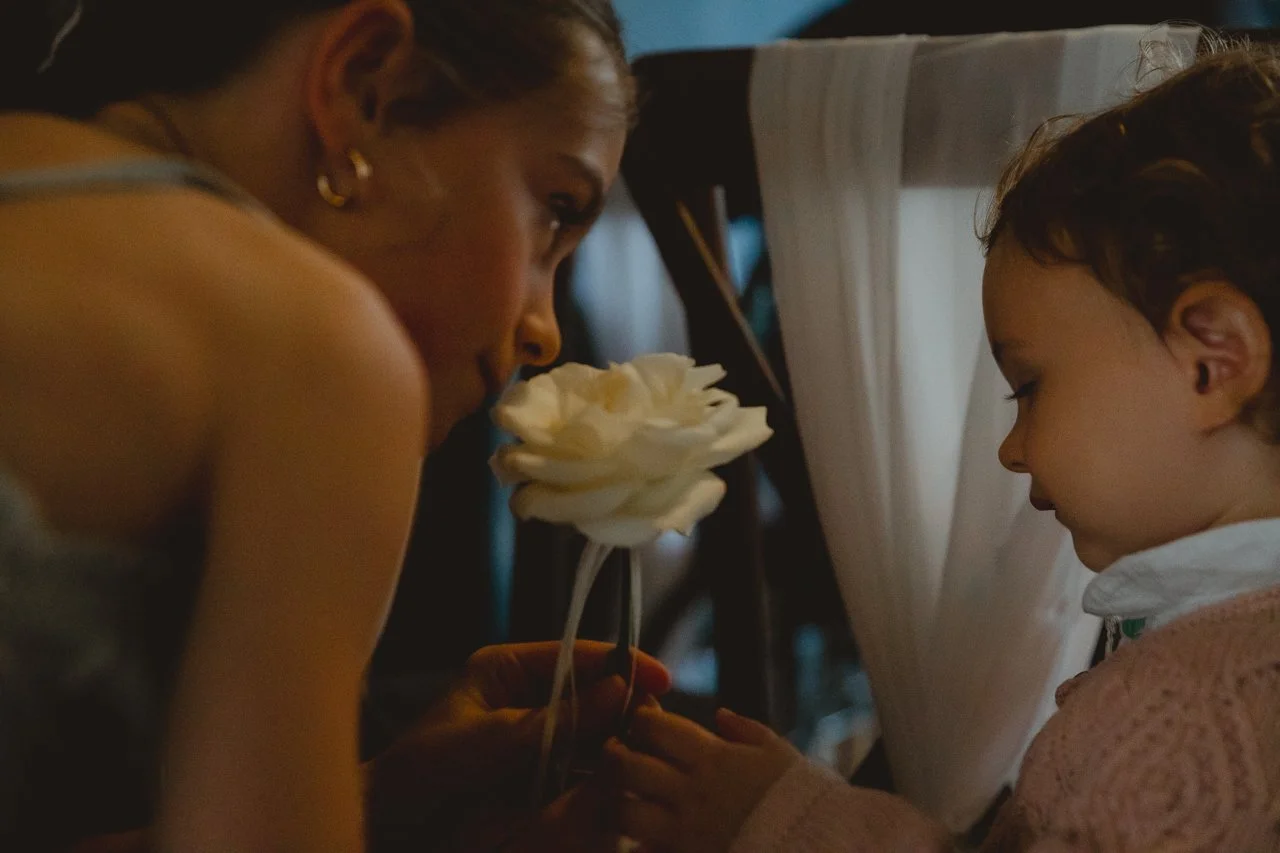 Young bridesmaid leans down in soft indoor lighting to give a white rose to a flower girl at The Georgian Townhouse Norwich Norfolk 