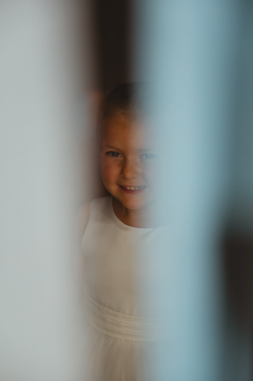 Young bridesmaid flowergirl seen between the window peering out at the sun at Georgian Townhouse Norfolk Norwich 