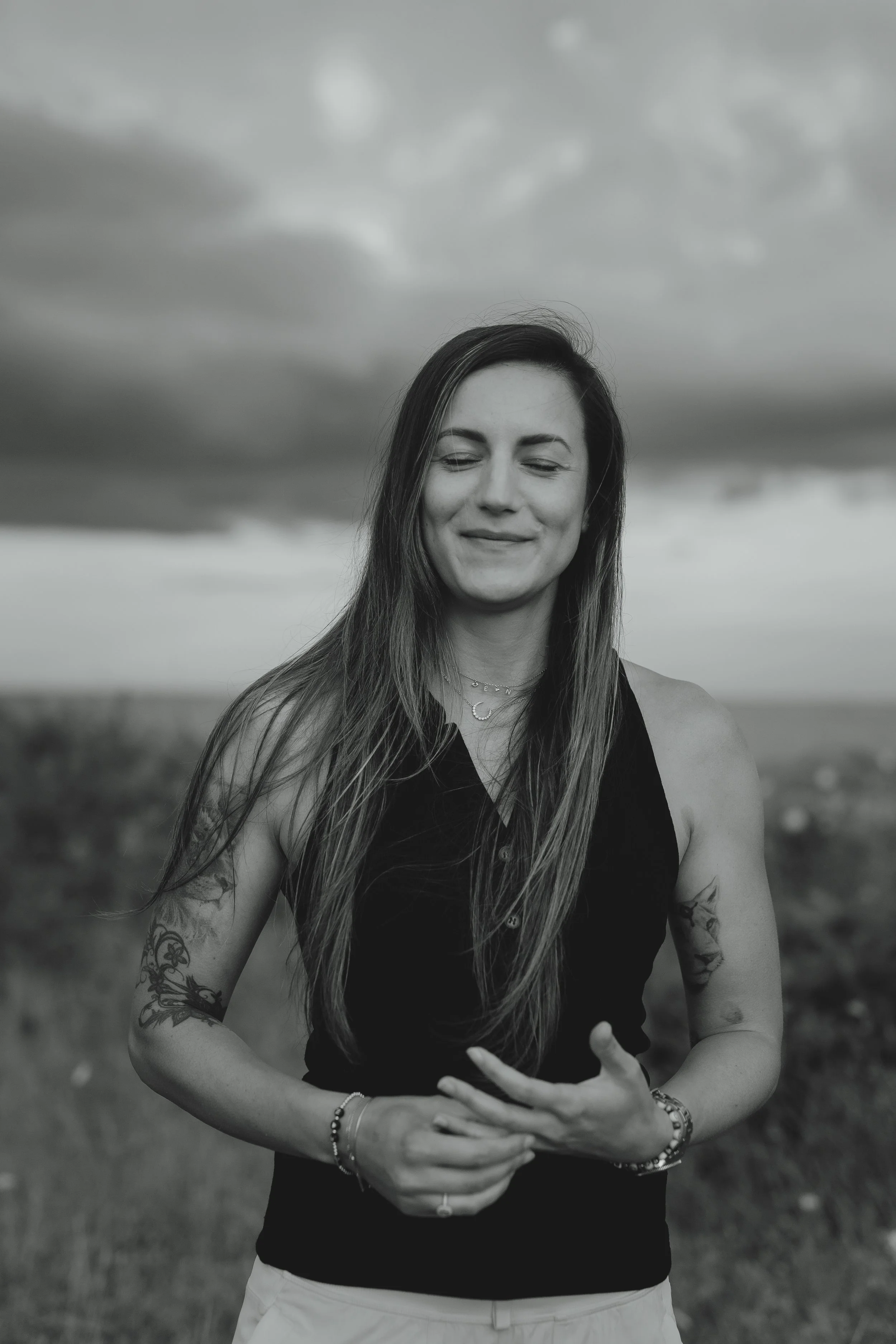 Black and white portrait of a tattooed woman staff portrait against a moody sky in Pakefield Suffolk 