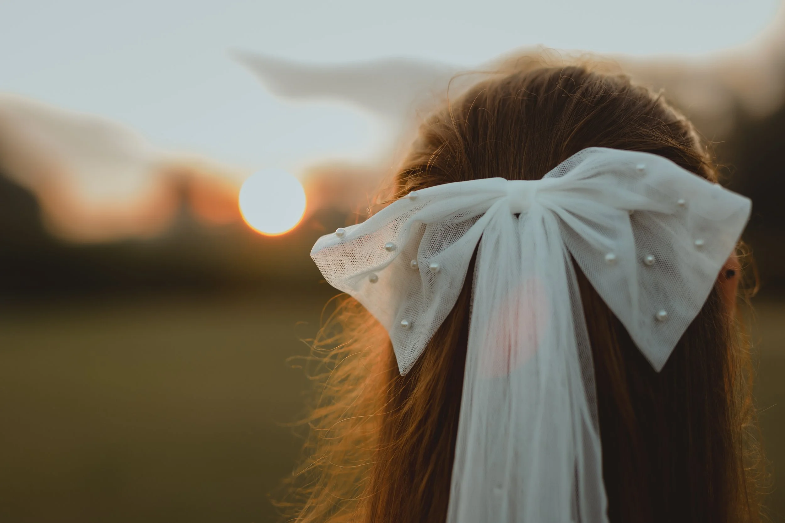 Abstract artistic image in the setting sun of a new bride looking out into the sunset with a bow in her hair at Sudbourne Hall Orford Suffolk Coast 