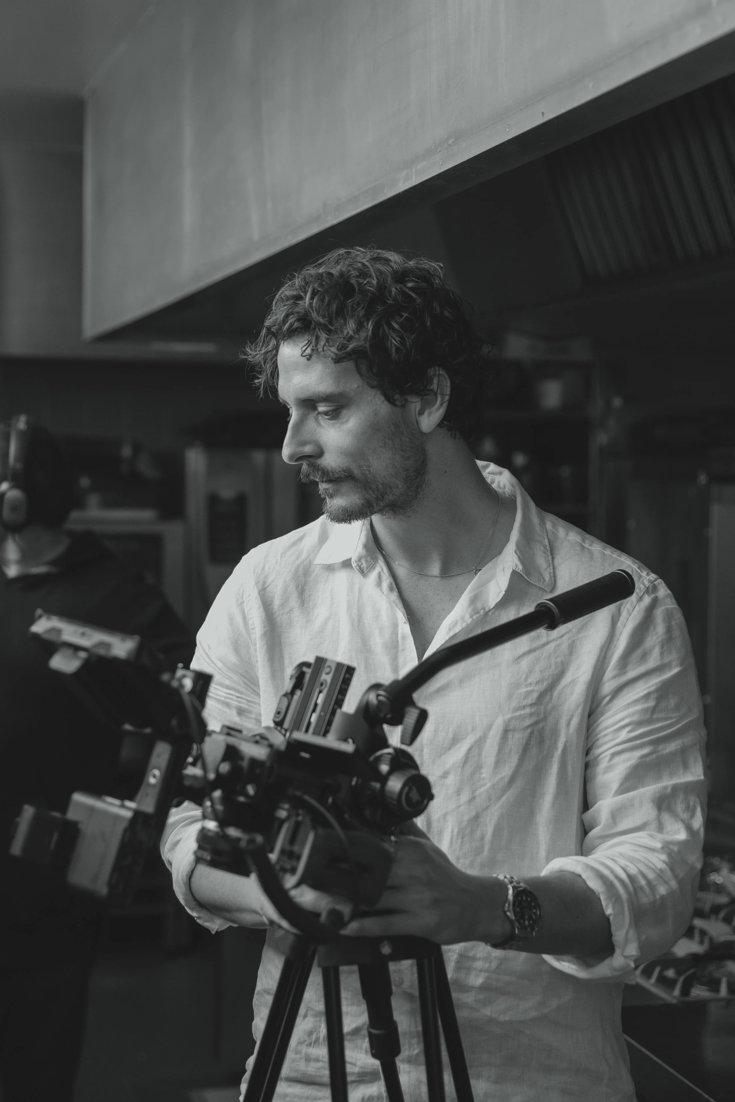 Male cinematographer with professional camera in white shirt looks down in black and white on location at Lowestoft Suffolk 