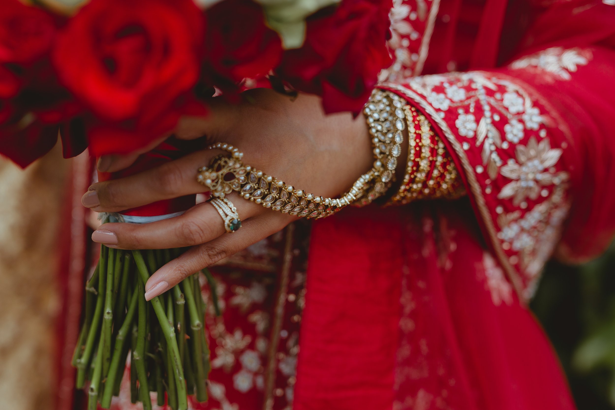 South Asian wedding close up of asian brides hand with golden bangles and jewellery and rings ad red and white roses at Wensum Golf Club Norwich Norfolk  