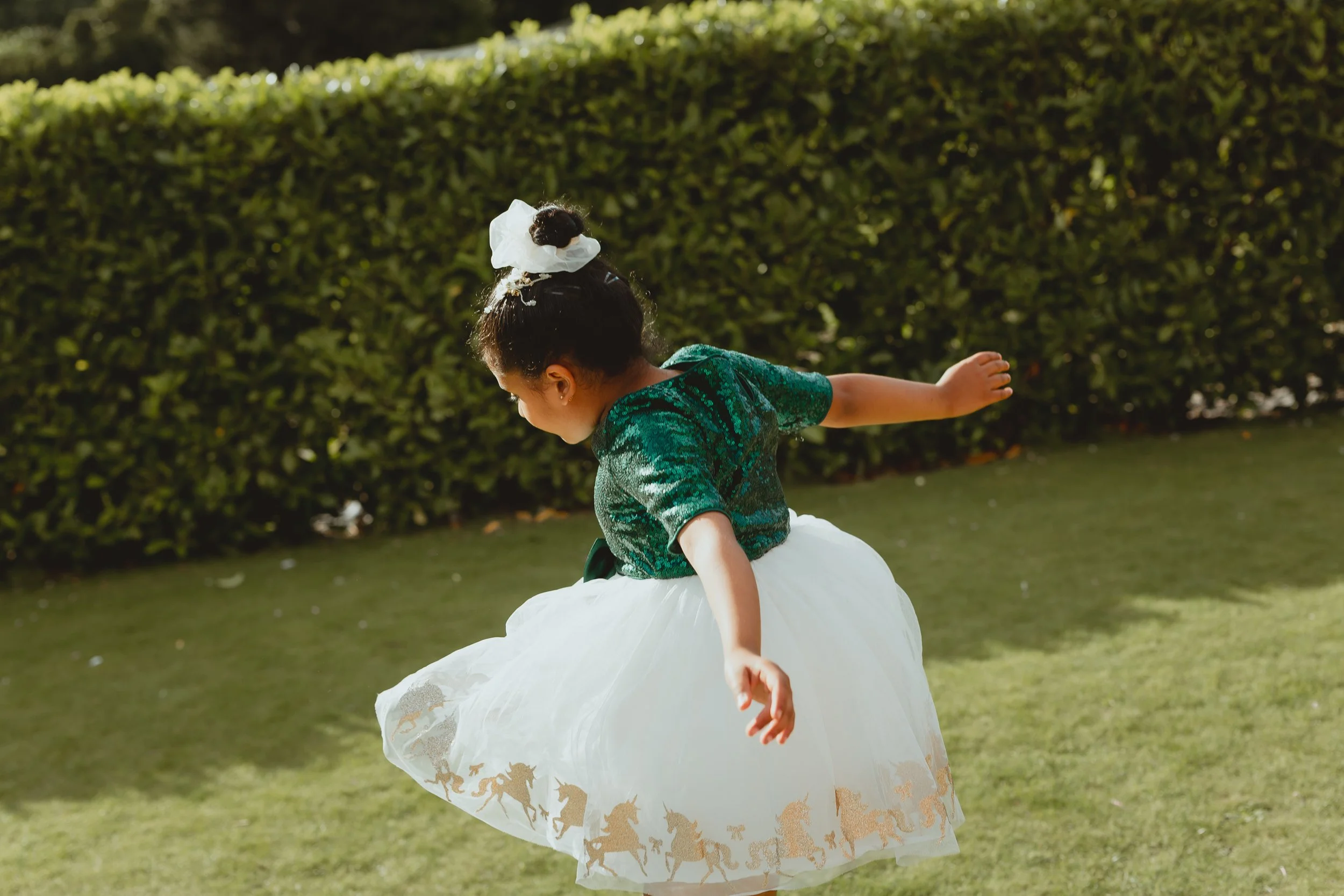 South asian wedding guest girl jumps for joy in the sun  in sequinned green top and white tutu with gold inlay detail at Wensum Valley Golf Club Norwich Norfolk