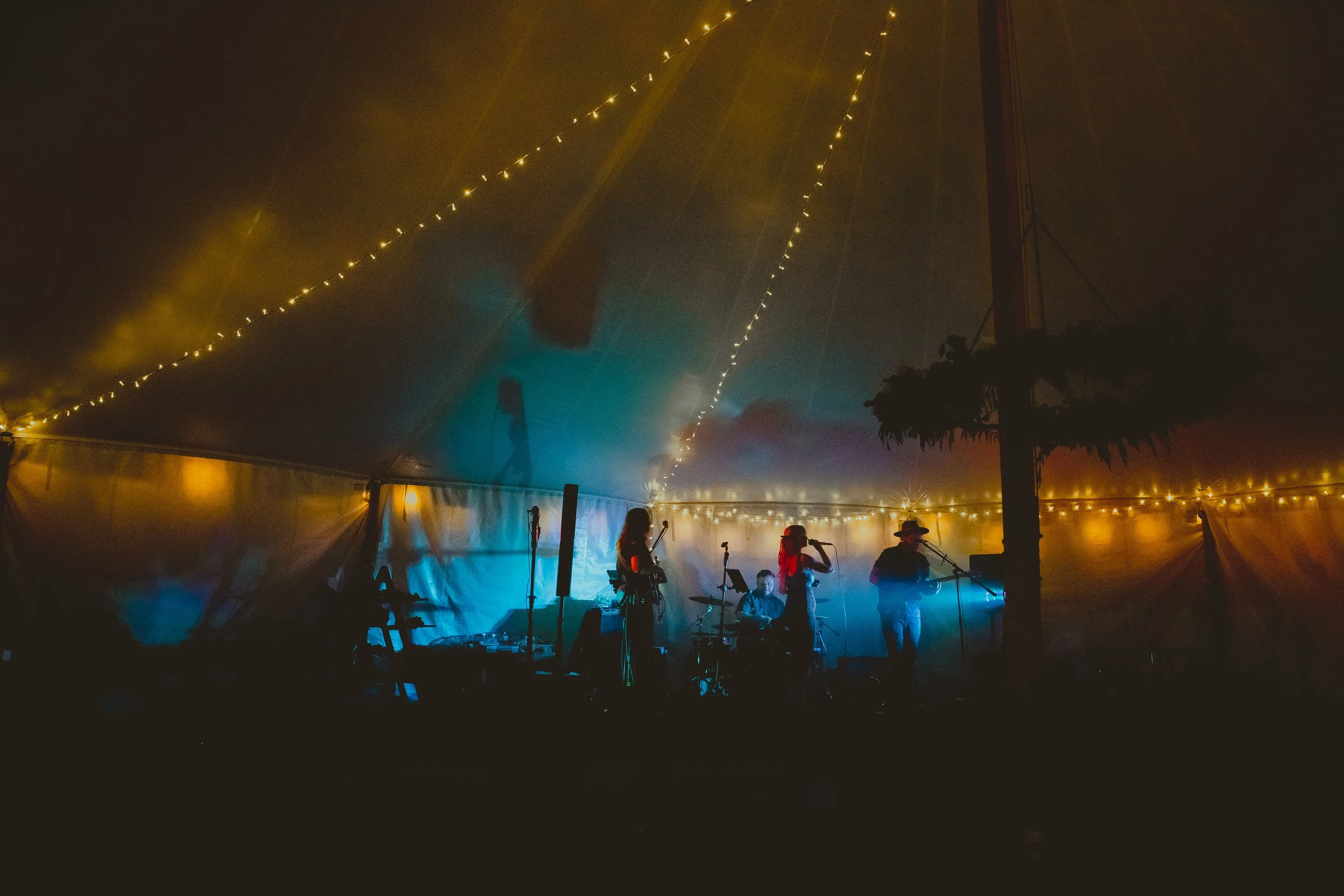 Dark cinematic atmospheric photograph of band playing inside a marquee at bohemian festival wedding with fairy and festoon lights with bright blue up lighting Blundeston Lowestoft Suffolk 
