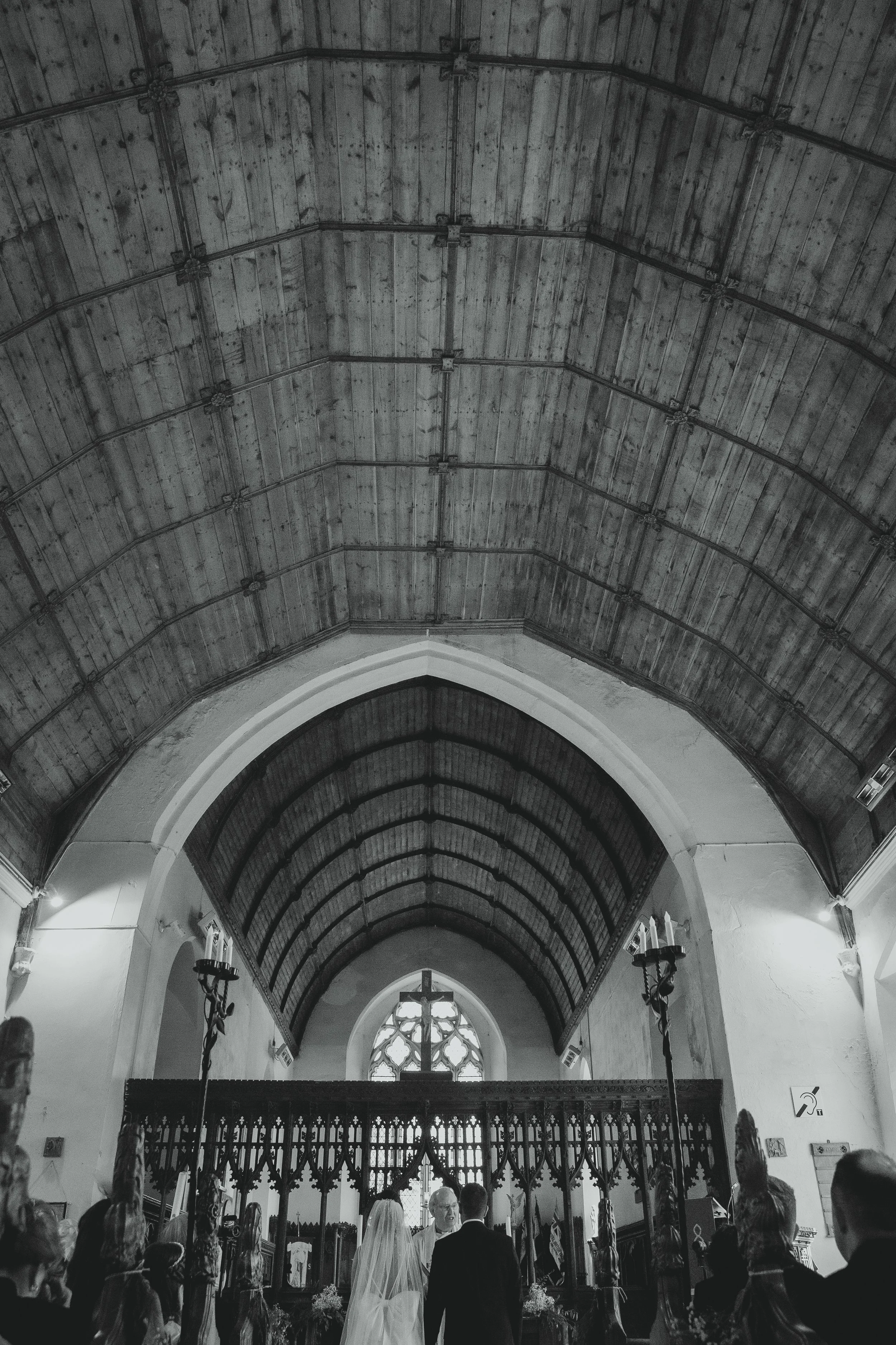 Documentary black and white wide shot focusing on the detailing and architecture in a church with a vicar at the front and a bride and groom stood before the pews at Blundeston church Lowestoft Suffolk 